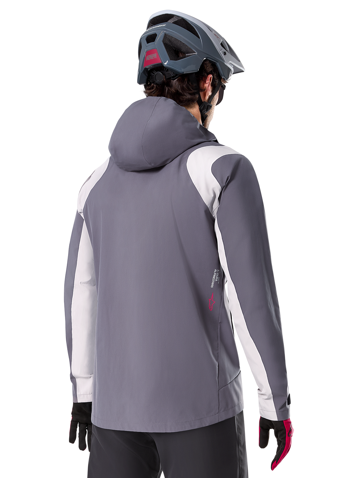 Alpinestars A-Dura Regenjacke, Mountainbike-Jacke, Dunkles Titangrau, Rückansicht mit hellgrauen Schulter- und Armeinsätzen, rotes Logo-Detail an der Seite, getragen mit einem grauen MTB-Helm und schwarz-roten Handschuhen, technische Trail-Bekleidung