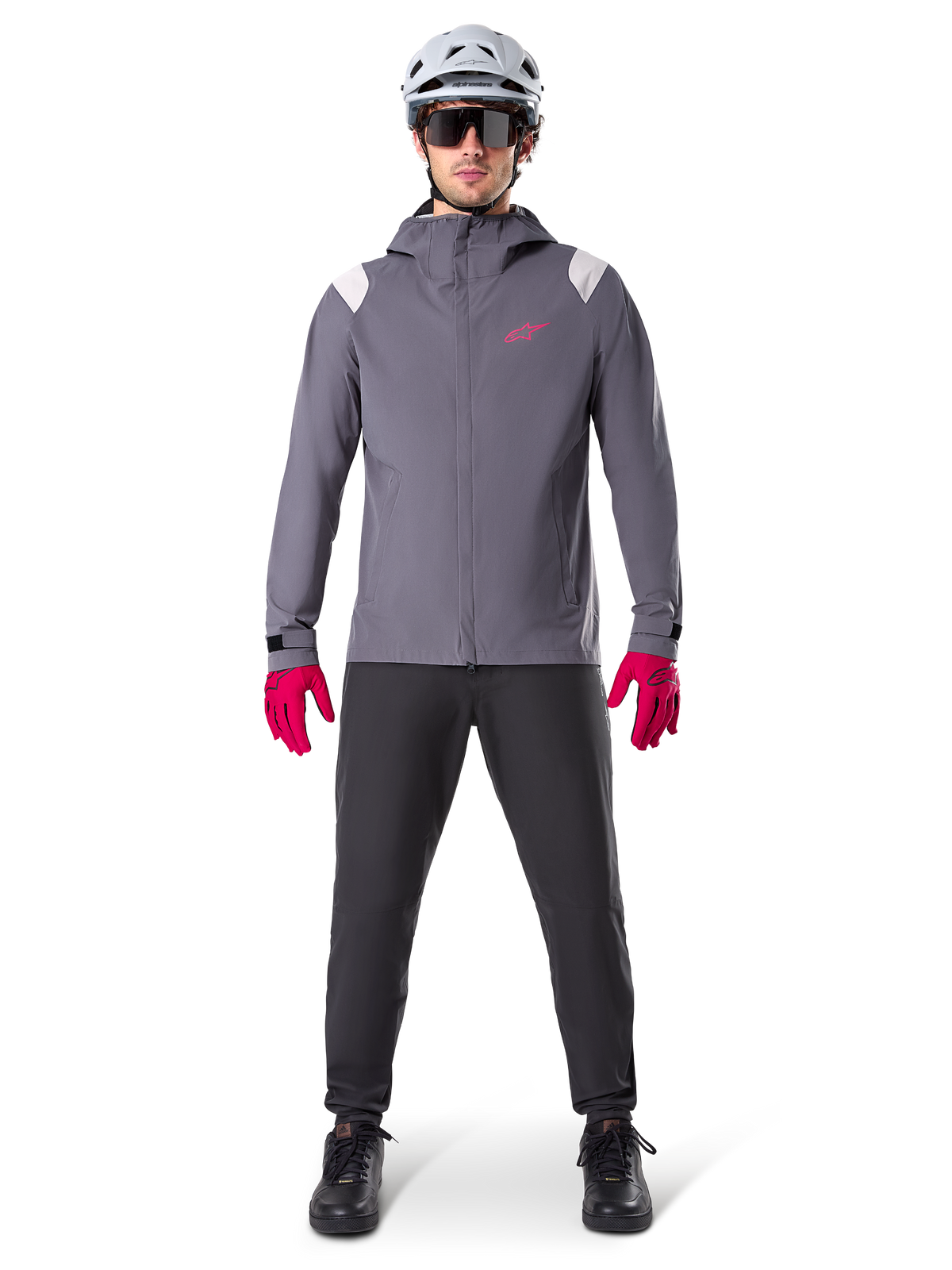 Alpinestars A-Dura Regenjacke, Mountainbike-Jacke, Dunkles Titangrau mit pinkem Logo, getragen mit grauem MTB-Helm und leuchtend pinken Handschuhen, schützendes 2,5-Lagen-Membran-Design für Radsport bei nassem Wetter