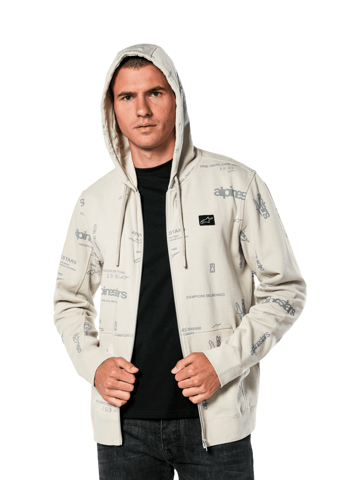 Alpinestars Plenitude Hoodie, lässige Sportbekleidung, Off-White Fleece mit Reißverschluss vorne und grauen Allover-Logo-Grafiken, getragen von einem Mann mit aufgesetzter Kapuze über einem schwarzen Shirt, kleiner Logo-Patch auf der Brust, Kängurutasche