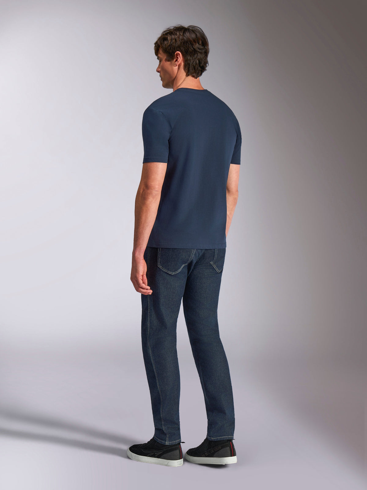 Alpinestars Ageless Shadow CSF Tee, kurzärmeliges T-Shirt, Marineblau, Rückansicht am Modell, getragen mit dunklen Denim-Jeans und schwarzen Sneakern, lässige Lifestyle-Streetwear