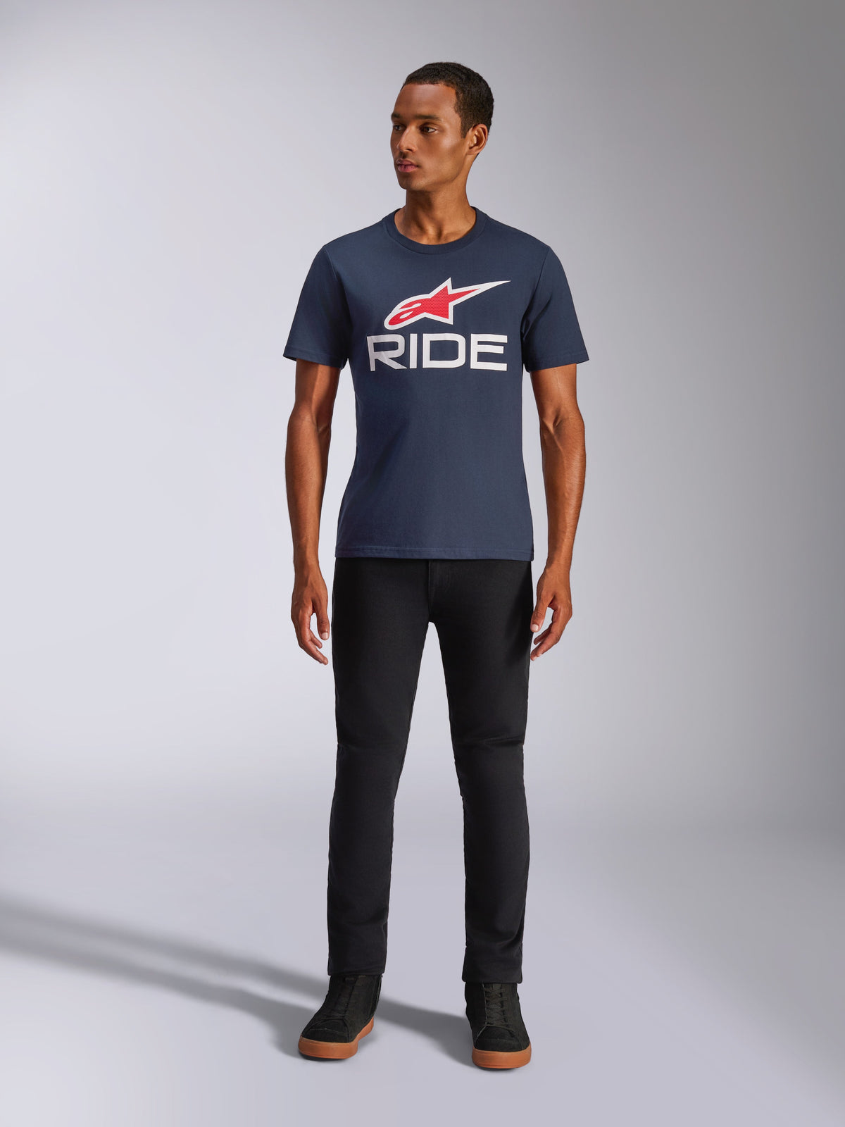 Alpinestars Ride 4.0 CSF Tee, kurzärmeliges T-Shirt, Marineblau mit rotem Alpinestars Stern-Logo und weißem 'RIDE'-Schriftzug auf der Brust, getragen von einem Model mit schwarzer Hose und schwarzen Sneakern, lässige, vom Motorsport inspirierte Streetwear