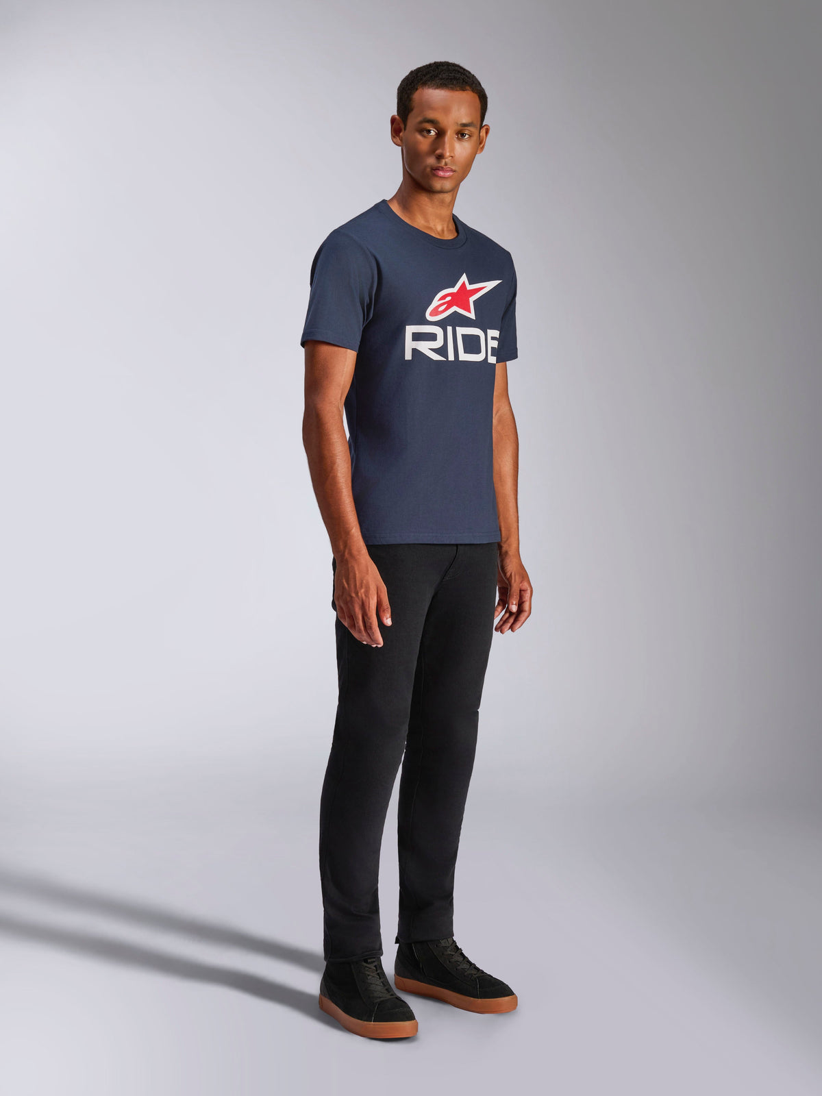 Alpinestars Ride 4.0 CSF Tee, Kurzarm-T-Shirt, Dunkelblau, weißes RIDE-Logo mit rotem Alpinestars-Stern, getragen von einem Model mit schwarzer Hose und Sneakern, lässige Motorsport-Lifestyle-Bekleidung