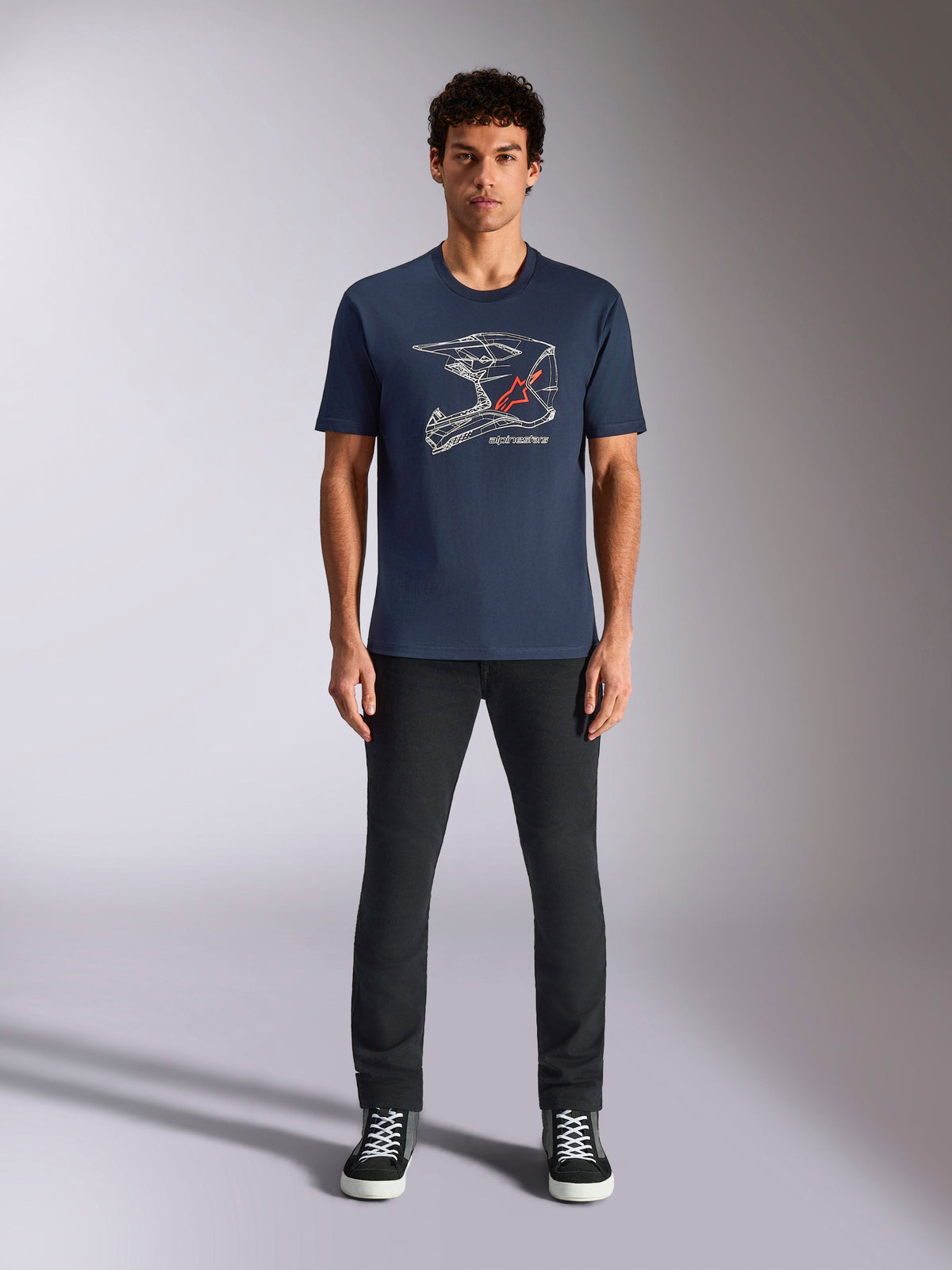 Alpinestars MX Helmet CSF Tee, kurzärmeliges T-Shirt, Marineblau, mit weißer Motocross-Helm-Grafik und rotem Stern-Logo, getragen von einem Model mit schwarzer Hose und Sneakern, lässige vom Motorsport inspirierte Streetwear
