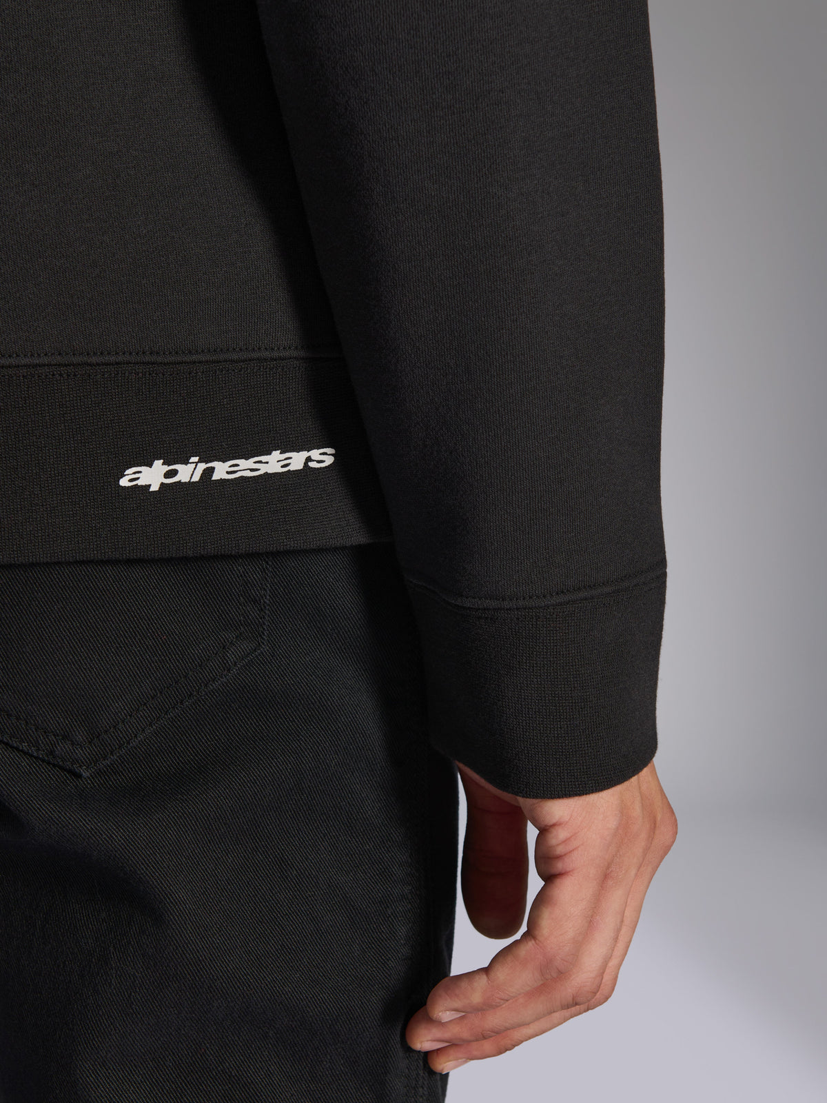Alpinestars Positive Crew, Black Pullover Sweatshirt, close-up detail of ribbed hem and sleeve cuff with white Alpinestars logo, premium fabric texture, casual motorsport-inspired sportswear