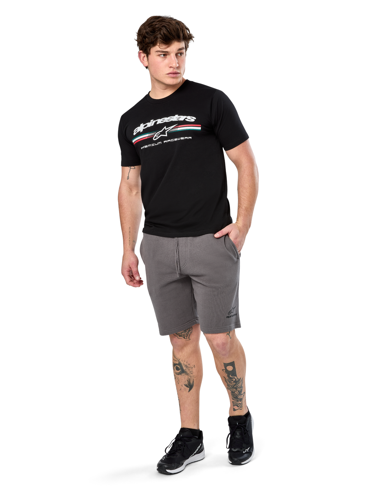 Alpinestars Prevail Csf Tee, Kurzarm-T-Shirt, Schwarz, weißes Alpinestars-Logo mit dreifarbigem Paddock-Streifen, kombiniert mit grauen Shorts und schwarzen Sneakern, lässige Motorsport-Streetwear