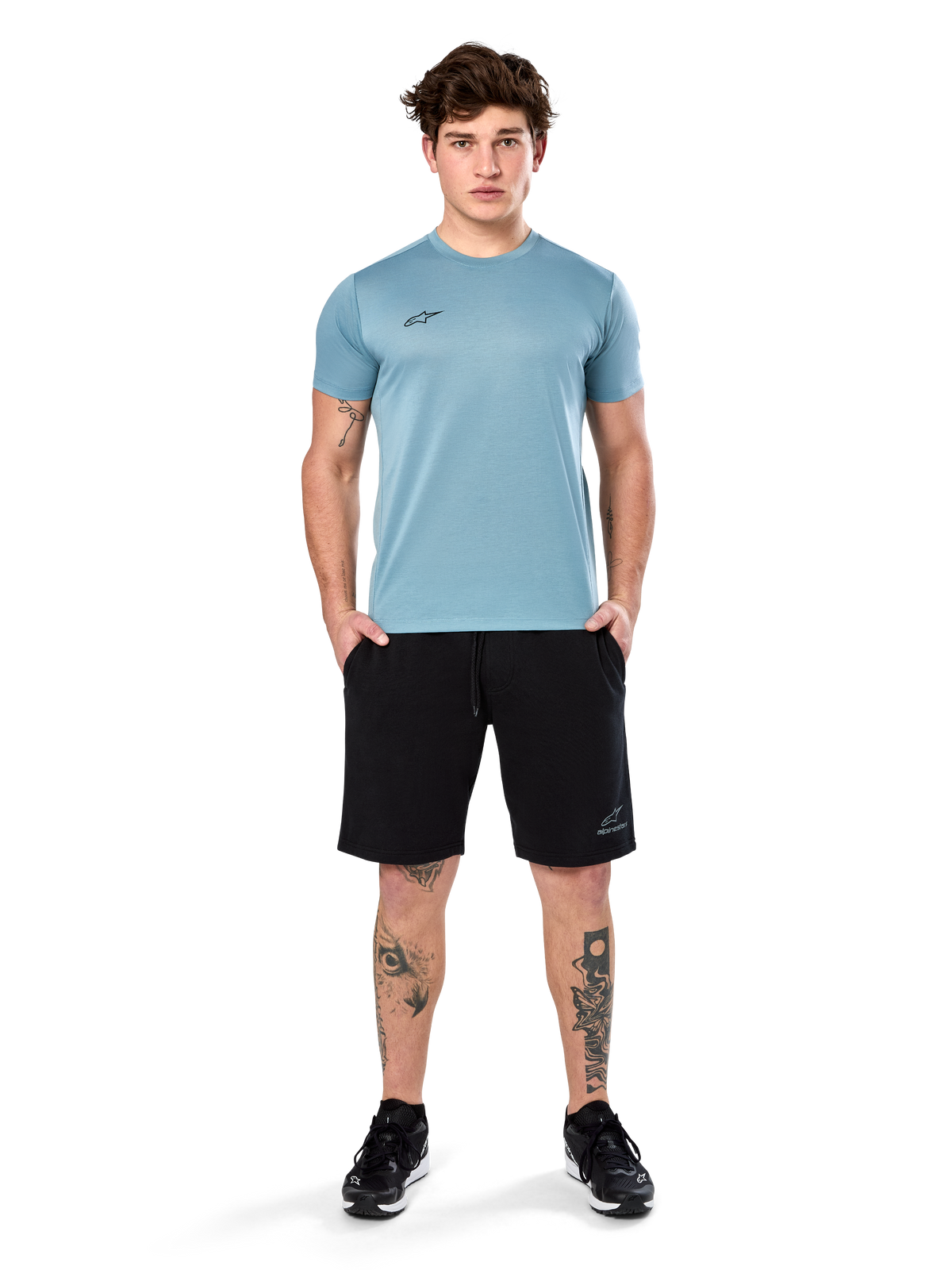 Alpinestars Point Performance Tee, Kurzarm-T-Shirt, Ice Blue, mit kleinem schwarzen Logo vorne, Rundhalsausschnitt, getragen von einem Model mit schwarzen Shorts und schwarzen Sneakern, lässige feuchtigkeitsableitende Sportbekleidung