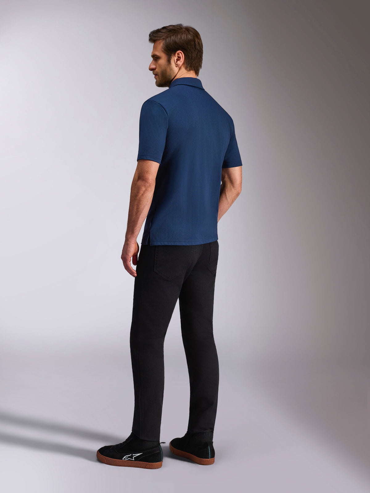 Alpinestars Impetus Sport Polo, kurzärmeliges Poloshirt in Marineblau, Rück- und Seitenansicht am Model, kombiniert mit schwarzer Hose und schwarzen Sneakern, lässige Motorsport-Lifestyle-Sportbekleidung