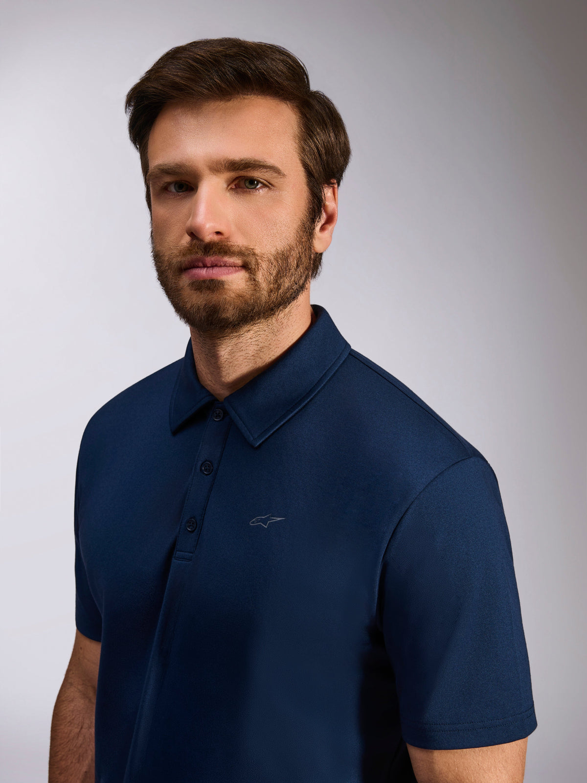 Model trägt Alpinestars Impetus Sport Polo, Navyblau, Kurzarm-Poloshirt aus Mock-Mesh, mit einer 3-Knopf-Leiste und dezentem Astars-Logo auf der Brust, lässige Motorsport-Lifestyle-Bekleidung