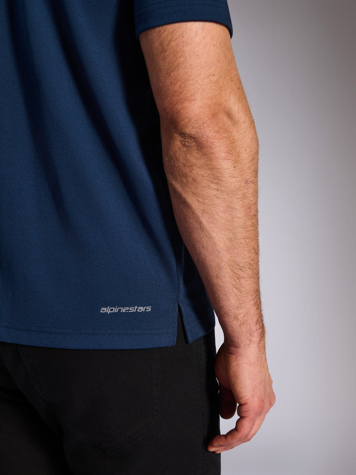 Alpinestars Impetus Sport Polo, Navy, Nahaufnahme des unteren Saums mit Alpinestars-Schriftzug und Seitenschlitz, Mock-Mesh-Strickstruktur, lässige Motorsport-Sportbekleidung