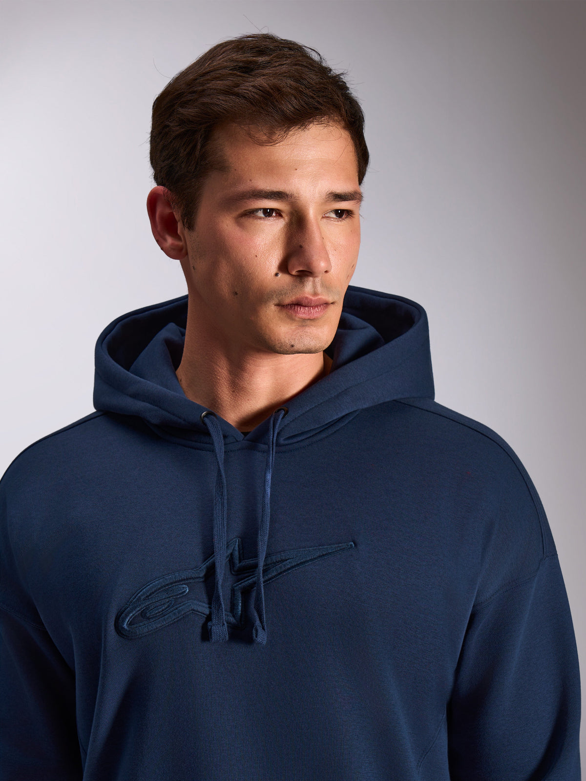 Alpinestars Emergent Oversized Hoodie, navy blue, close-up of model wearing pullover fleece hoodie, featuring tonal 3D embroidered Astars logo on the chest, adjustable drawstring hood, casual motorsport streetwear