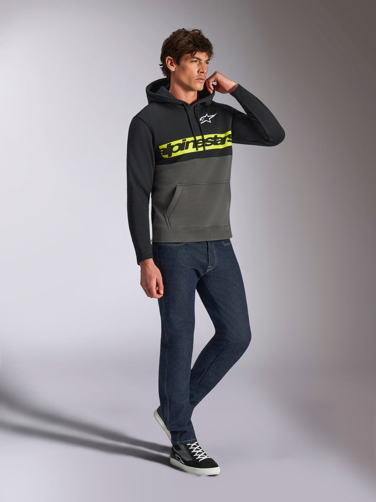 Alpinestars Parallel Hoodie, lässige Streetwear, Color-Block-Design in Schwarz und Gunmetal-Grau, neongelber Alpinestars-Schriftzug auf der Brust, weißes Astars-Logo, Kapuze mit Kordelzug, getragen mit dunklen Jeans und Sneakern