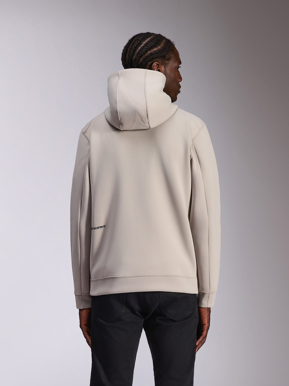 Alpinestars Cypher Hoodie, lässige Sportbekleidung, Zementgrau, Rückansicht am Modell, hochgeschlossene Kapuze, Doubleface-Fleece-Material, minimales Alpinestars-Logo am unteren Rücken, kombiniert mit schwarzer Hose