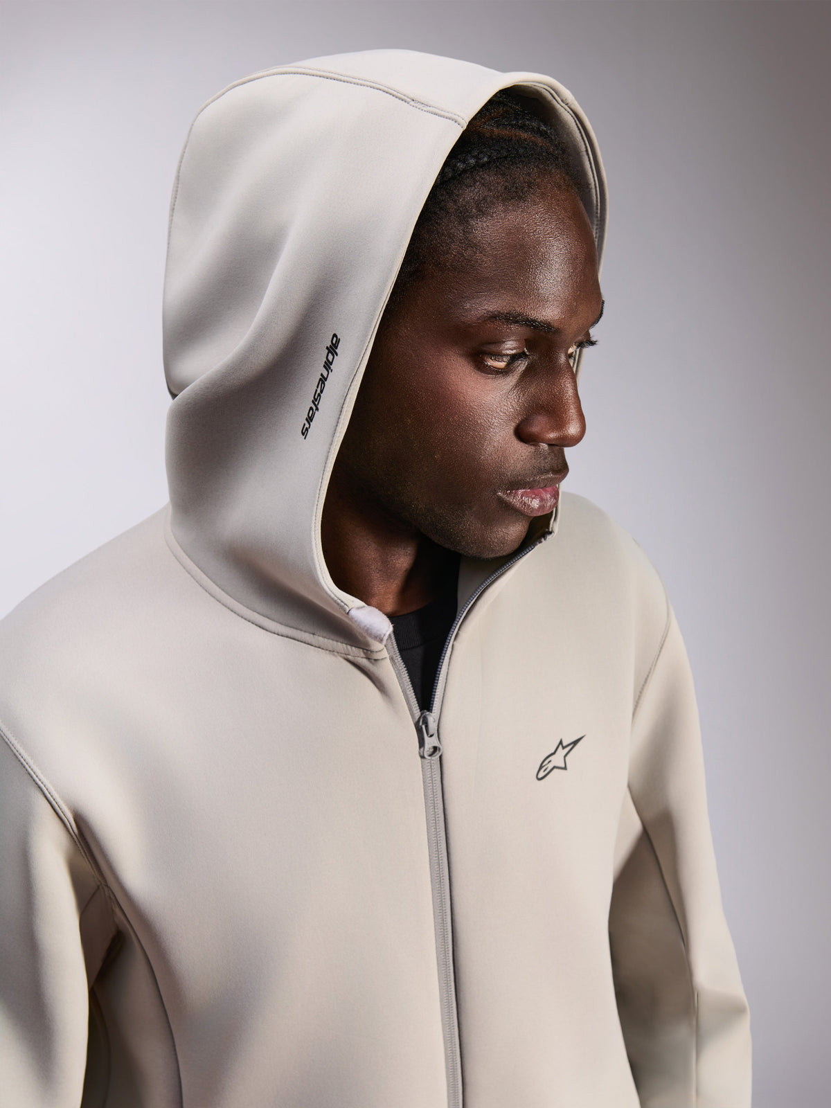 Alpinestars Cypher Hoodie, Zip-up Fleece-Hoodie, Zementgrau, getragen mit aufgesetzter Kapuze, Alpinestars-Wortlogo auf der Kapuze und kleines Astars-Logo auf der Brust, lässige, vom Motorsport inspirierte Streetwear