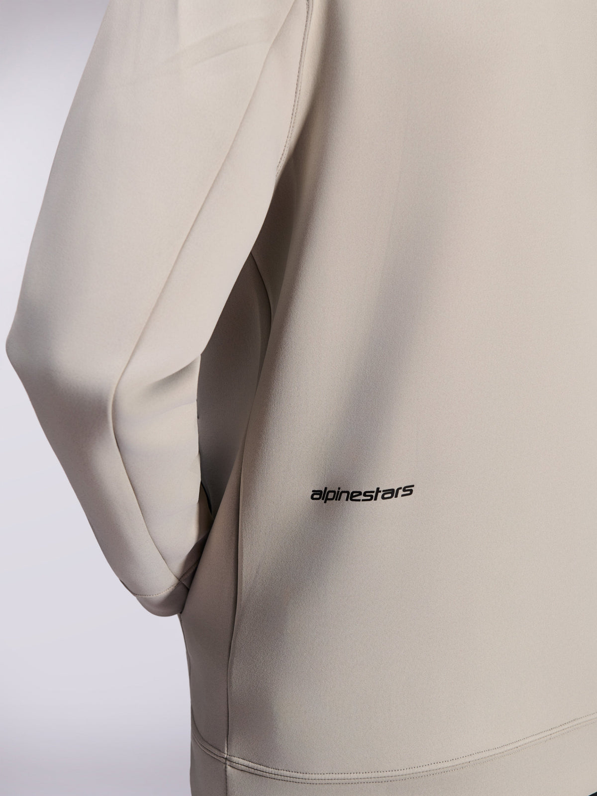 Alpinestars Cypher Hoodie, Zip-Hoodie aus Double-Face-Fleece, Cement Gray, Nahaufnahme des kleinen schwarzen Alpinestars-Wortlogos am unteren Rücken, Detail einer Nahttasche und glatte Stofftextur
