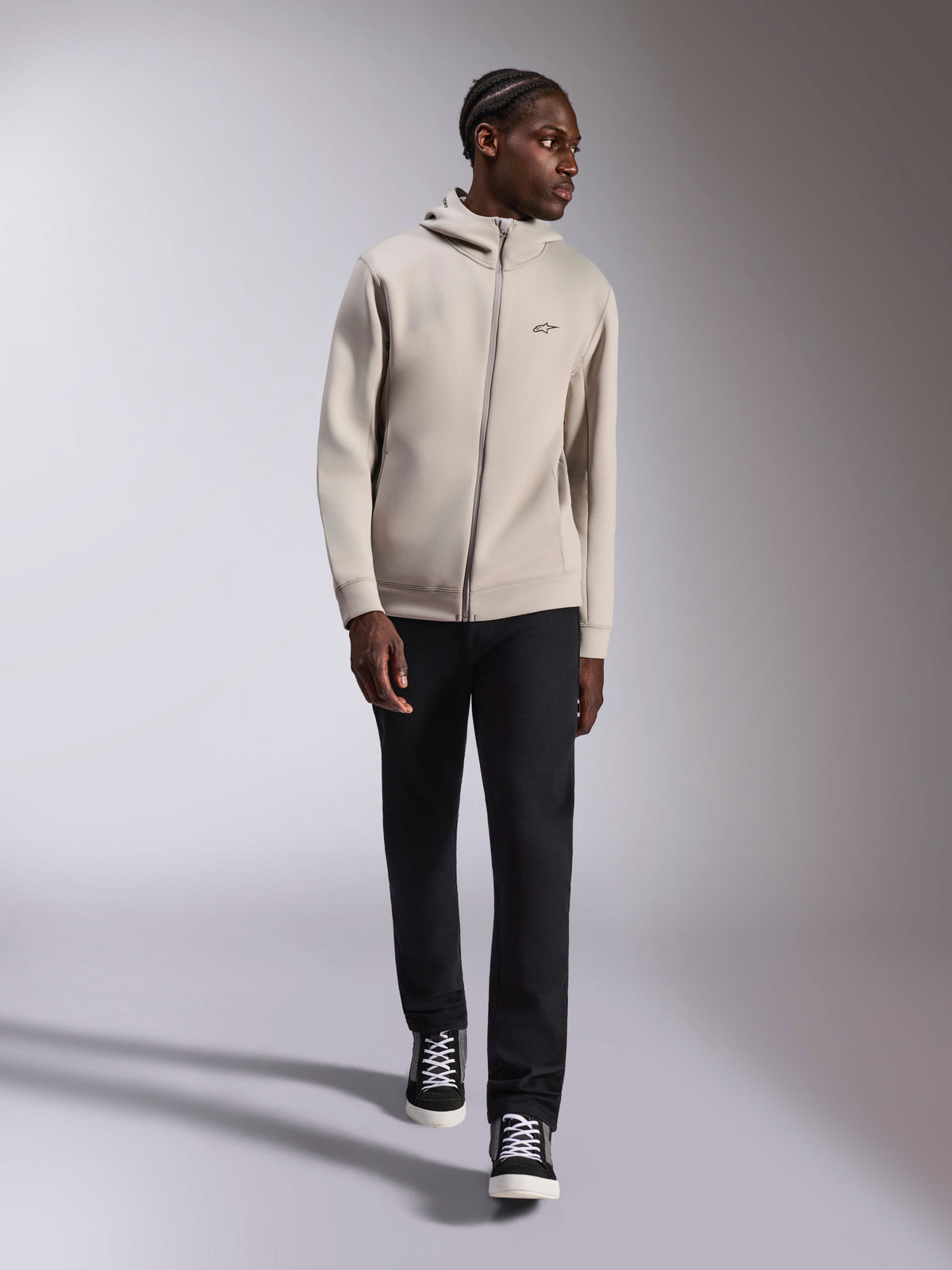 Alpinestars Cypher Hoodie, Full-Zip-Doppelvlies-Hoodie in Cement Gray, getragen von einem Model mit schwarzer Hose und schwarz-weißen Sneakern, mit hochgeschlossener Kapuze mit Mesh-Futter und kleinem Astars-Logo auf der Brust, moderne Streetwear