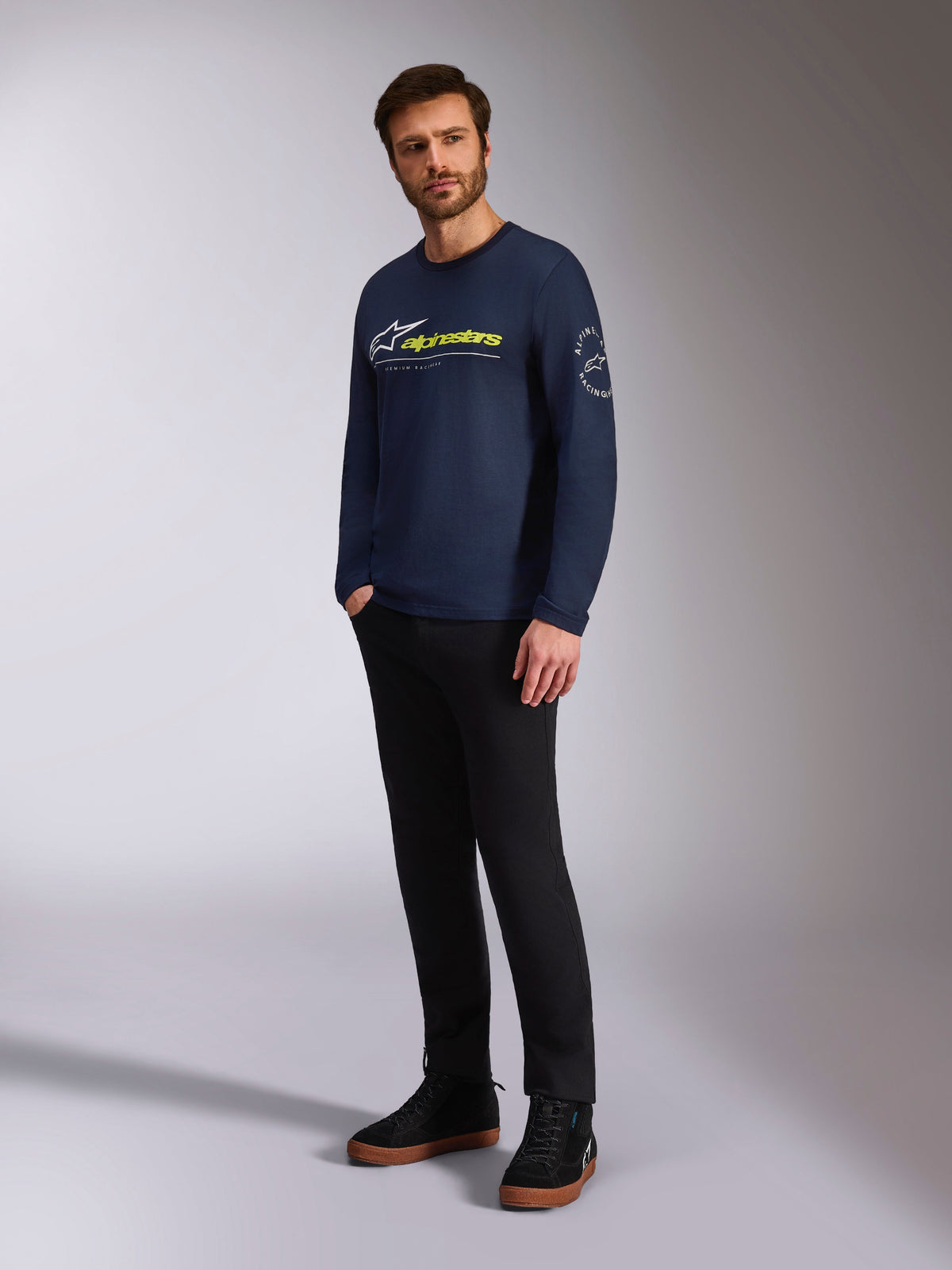 Alpinestars Mandatory CSF Tee, Langarmshirt, Navy, mit weißem Astars-Logo vorne und gelbem Alpinestars-Branding, Astars-Kreislogo am Ärmel, getragen von einem Model mit schwarzer Hose und schwarzen Sneakern für einen lässigen Lifestyle-Look