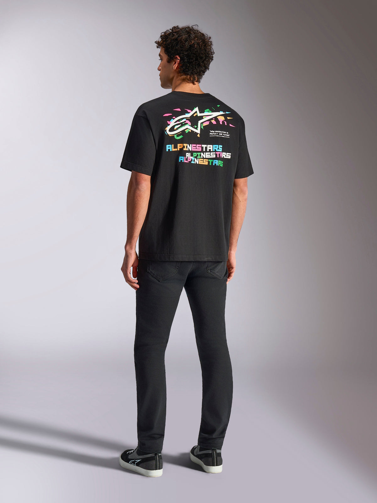 Alpinestars Wild Oversized CSF Tee, Kurzarm-T-Shirt, Schwarz, mit einer großen mehrfarbigen Grafik auf der Rückseite mit Astars-Logo und buntem Schriftzug, Oversized-Passform, getragen mit schwarzer Slim-Fit-Hose für einen lässigen Streetwear-Look