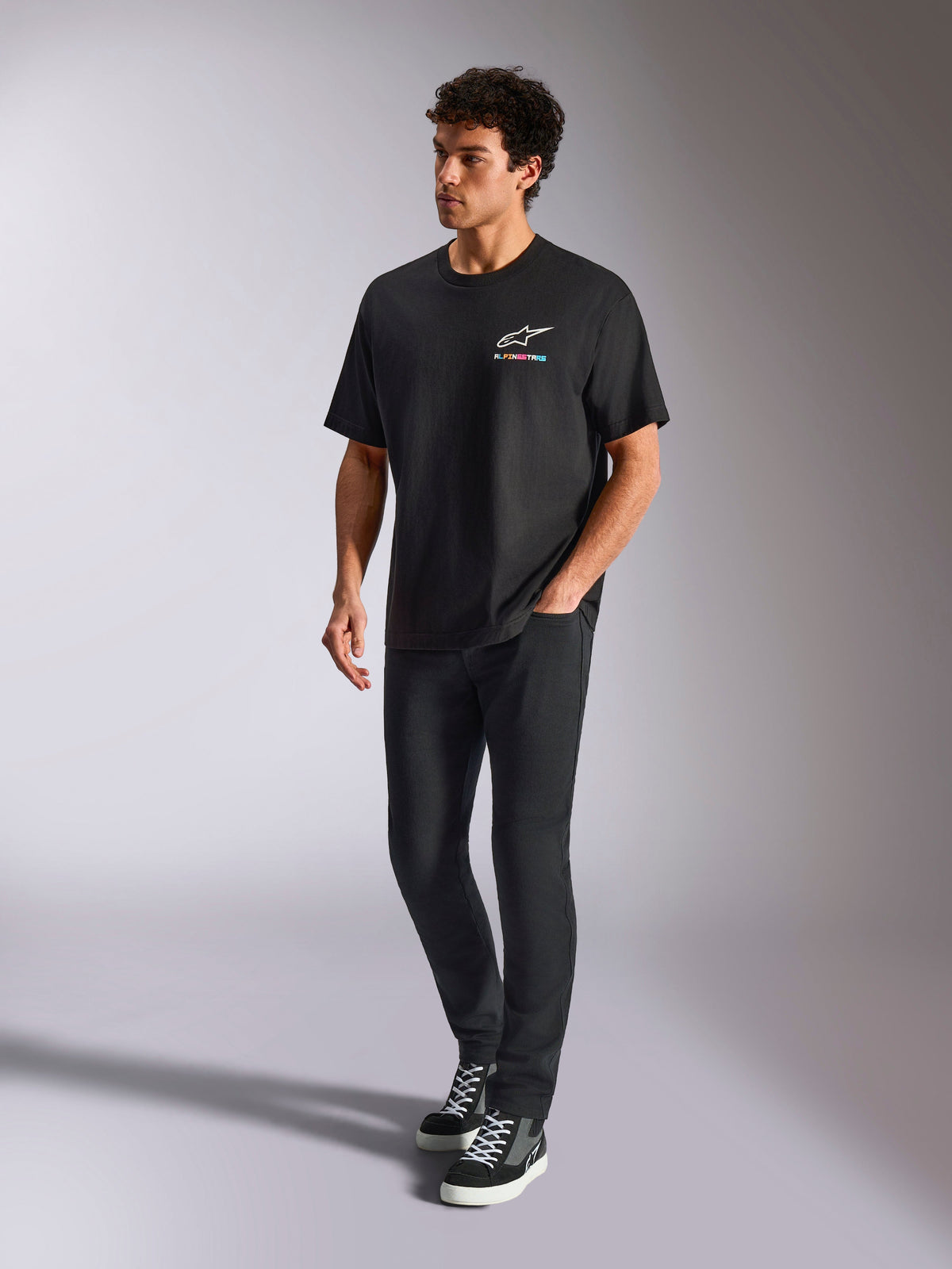 Alpinestars Wild Oversized CSF Tee, kurzärmeliges T-Shirt, Schwarz, mehrfarbiges Astars-Logo auf der Brust, lässiger Streetwear-Stil, getragen von einem Model mit schwarzer Hose und High-Top-Sneakern