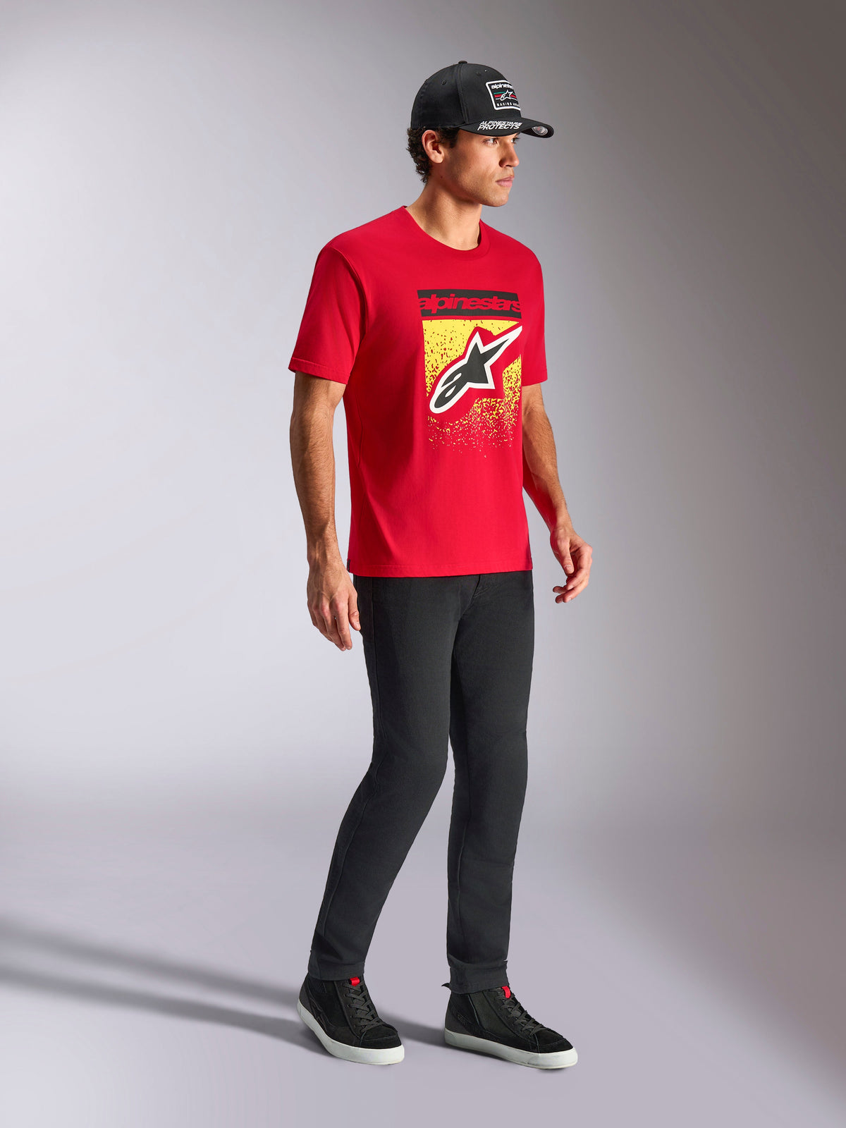 Alpinestars Noka CSF Tee, Kurzarm-T-Shirt, Rot, mit vorderseitigem Astars-Logo und MX-Verlauf auf einer gelben Grafik, getragen mit einer schwarzen Alpinestars-Kappe und schwarzer Hose, lässige Motorsport-Streetwear