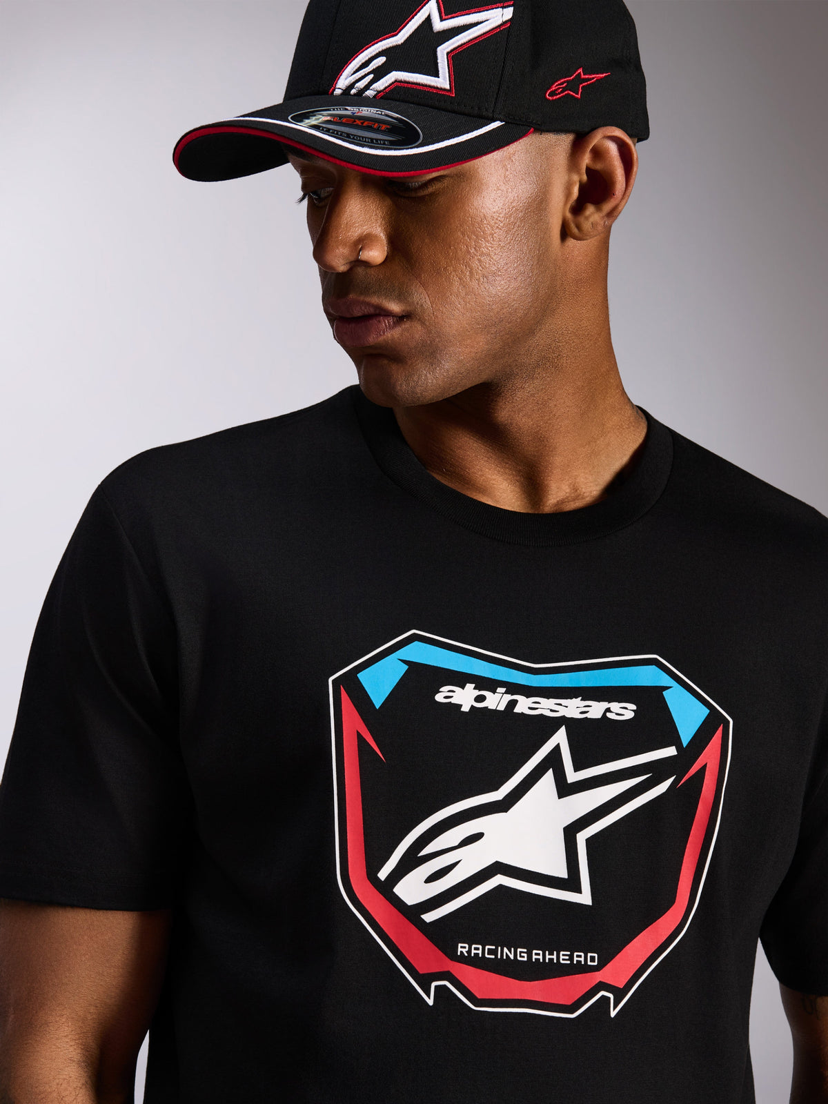 Alpinestars Plate CSF Tee, Short Sleeve T-Shirt, Black, Large Front MX Plate Graphic with Star Logo and Red and Blue accents, worn with a matching black Alpinestars cap, Casual Motorsport Streetwear