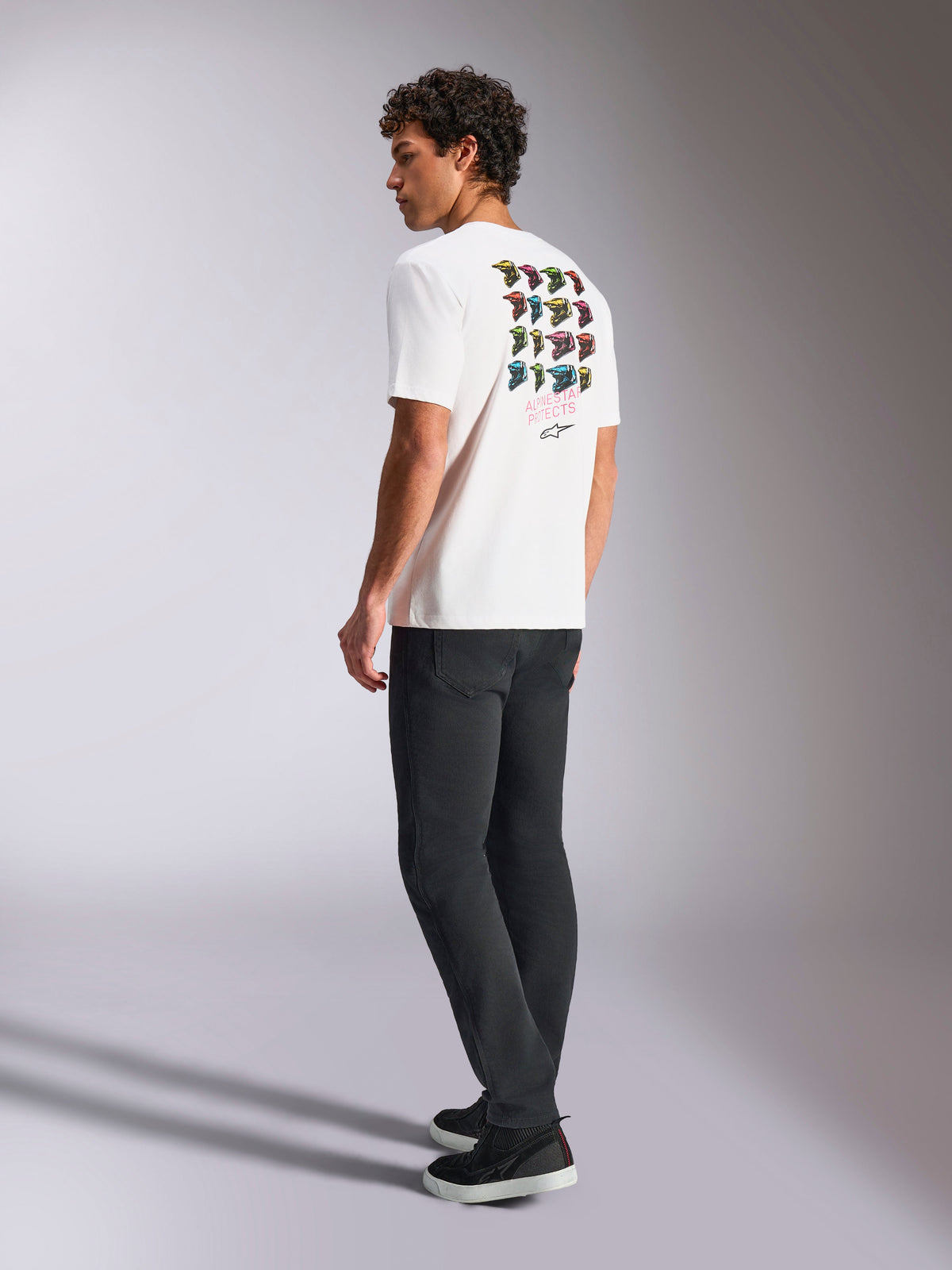 Alpinestars Pop Helmet CSF Tee, Short Sleeve T-Shirt, White, back view on model showing colorful M10 helmet graphic art, styled with dark pants and black sneakers, casual motorsport-inspired streetwear