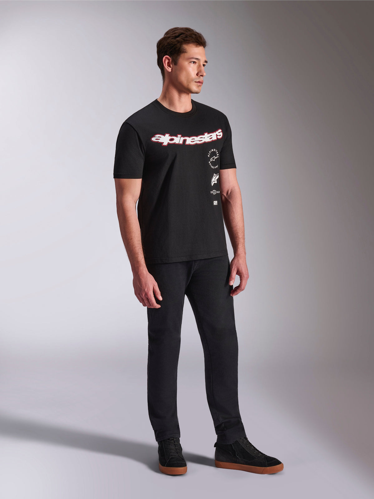 Alpinestars Abus CSF T-Shirt, kurzärmeliges T-Shirt, Schwarz, mit geschwungenem rot-weißen Alpinestars-Logo und vertikal gestapelten Grafiken, getragen mit schwarzer Hose und Sneakern, lässige motorsport-inspirierte Streetwear