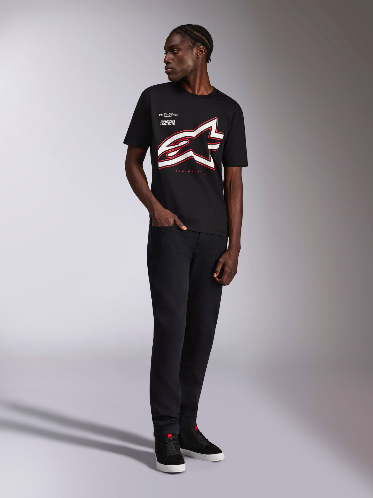 Alpinestars Authority CSF Tee, kurzärmeliges T-Shirt, Schwarz, großes rot-weißes angeschnittenes Astars-Logo als Umriss, getragen von einem Model mit schwarzer Hose und Sneakern, lässige Motorsport-Streetwear