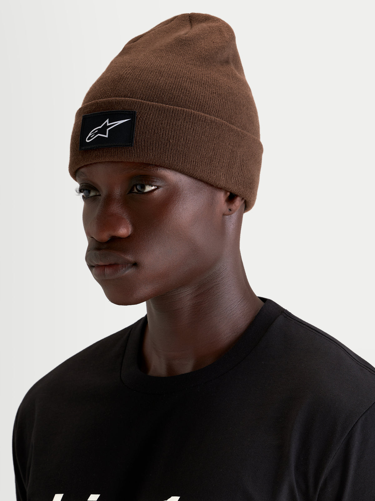 Alpinestars Augment Cuff Mütze, braune Sportswear-Strickmütze mit schwarzem und weißem Alpinestars Logo-Patch am Saum, getragen von einem Model