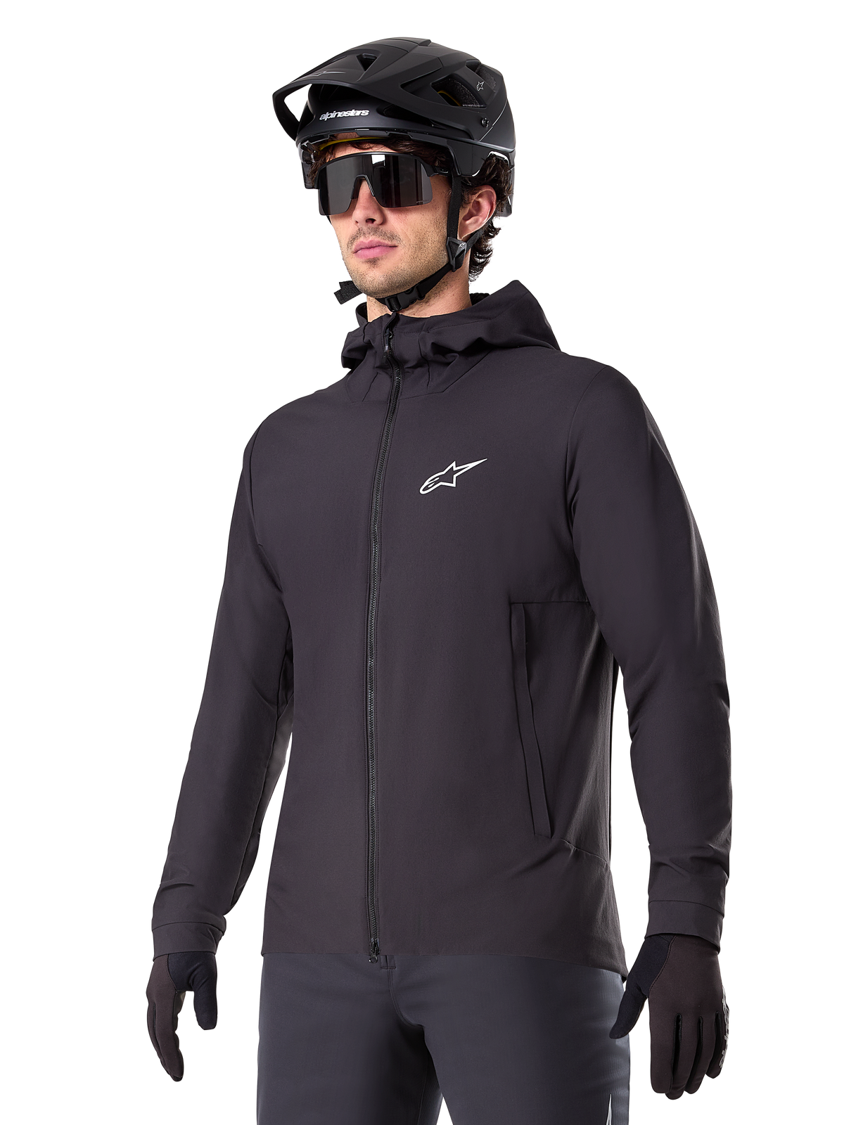 Alpinestars A-Dura Thermal Jacket, schwarze Fahrradjacke, Design mit Kapuze und Frontreißverschluss, weißes Stern-Logo auf der Brust, getragen mit schwarzem Mountainbike-Helm und Handschuhen, sportliche Funktionsbekleidung für Trailfahrten bei kaltem Wetter