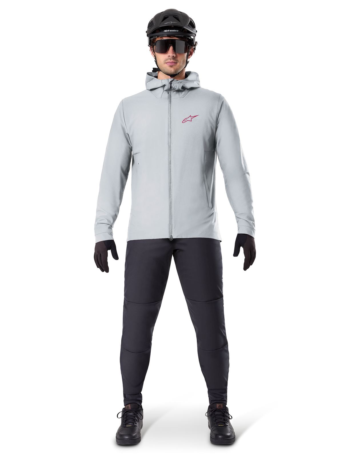 Alpinestars A-Dura Thermojacke, Titanium-Grau, Fahrradjacke getragen mit schwarzer Mountainbike-Hose, Handschuhen und Helm, mit einem kleinen roten Stern-Logo auf der Brust und einem durchgehenden Frontreißverschluss, leichte isolierte Ausrüstung für Offroad-Einsätze.