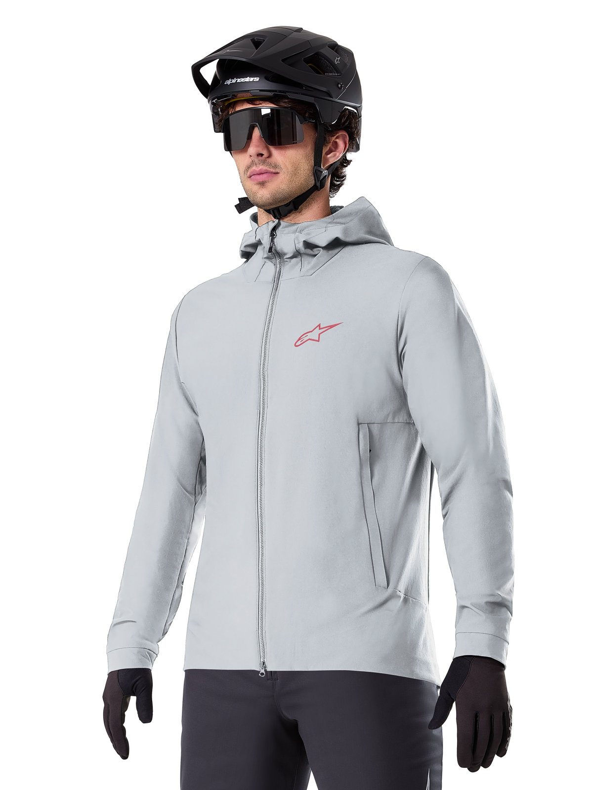 Alpinestars A-Dura Thermojacke, hellgraue isolierte Fahrradjacke, Kapuzendesign mit kleinem rotem Logo, getragen mit schwarzem Helm und Handschuhen, technische Mountainbike-Bekleidung für Fahrten bei kaltem Wetter
