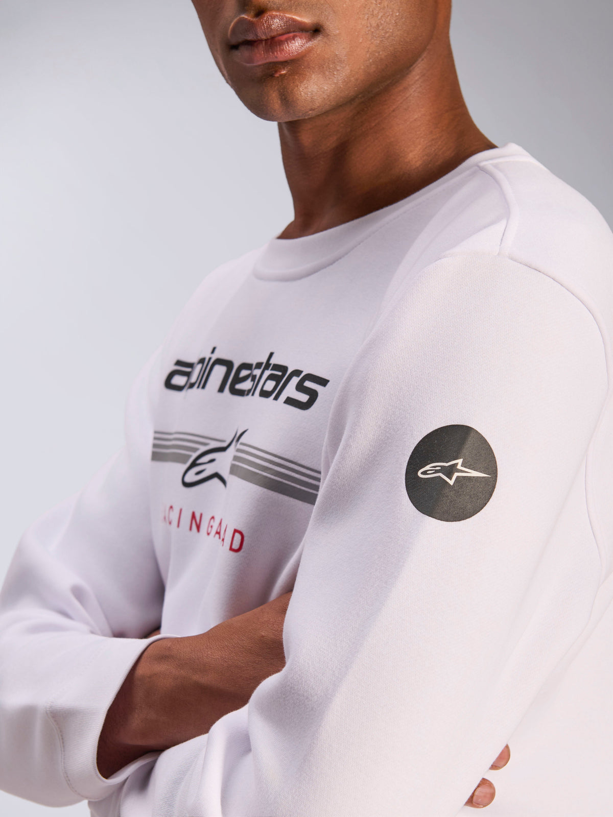 Alpinestars Bettern Crew, weißes Sweatshirt mit Rundhalsausschnitt, lässige Motorsport-Streetwear, Frontgrafik mit Alpinestars Wortmarke und grauen Streifen, schwarzer runder Stern-Logo-Patch am Ärmel, Fleece-Pullover