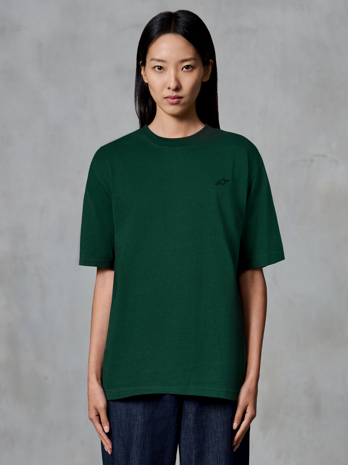 Alpinestars Essentials Ageless SS Tee, kurzärmeliges T-Shirt, Kieferngrün, von einem Modell getragen, mit kleinem schwarzen Logo auf der Brust, entspannte Passform, lässige Streetwear aus Bio-Baumwolle