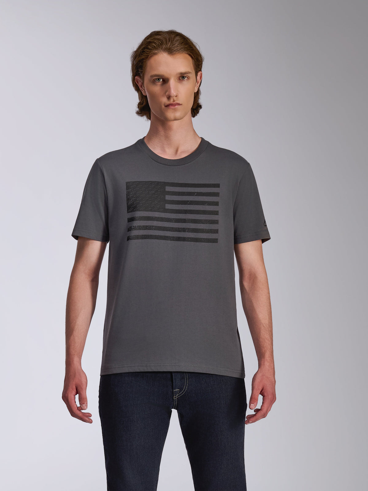 Alpinestars Waving CSF T-Shirt, Kurzarm-T-Shirt, Anthrazit, mit einer schwarzen, von einer Flagge inspirierten Blaze-Logo-Grafik auf der Brust, getragen von einem Modell mit dunklen Jeans, lässige Motorsport-Streetwear