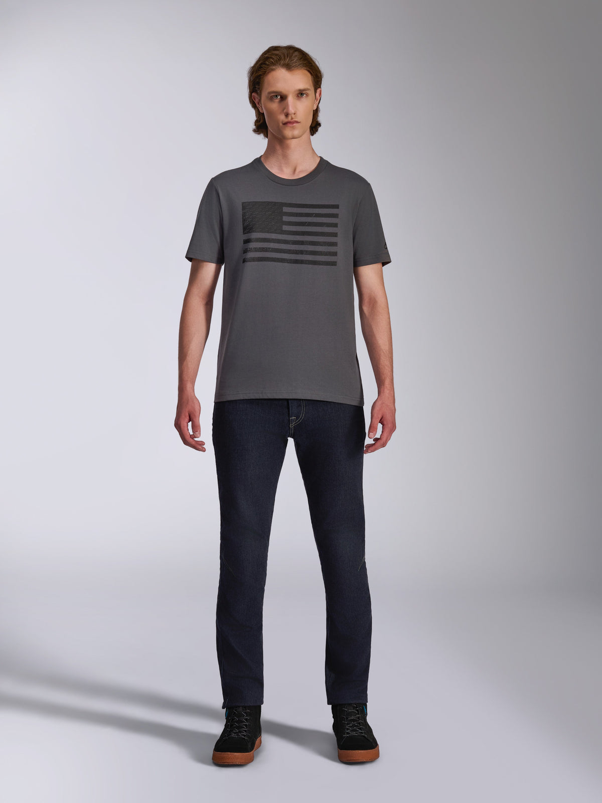 Alpinestars Waving CSF Tee, Kurzarm-T-Shirt, Anthrazitgrau, schwarze Blaze 2.0 Grafik im Flaggen-Stil, lässige Motorsport-Streetwear, getragen mit dunklen Denim-Jeans