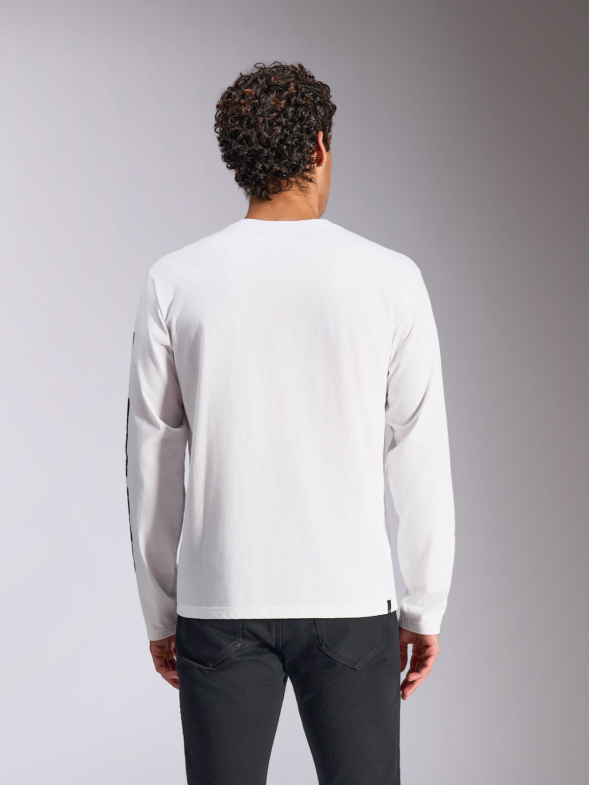 Alpinestars Trackside CSF Langarm-T-Shirt, Weiß, Rückansicht am Modell, kombiniert mit schwarzer Hose, reiner weißer Stoff mit langen Ärmeln, lässige, vom Motorsport inspirierte Streetwear