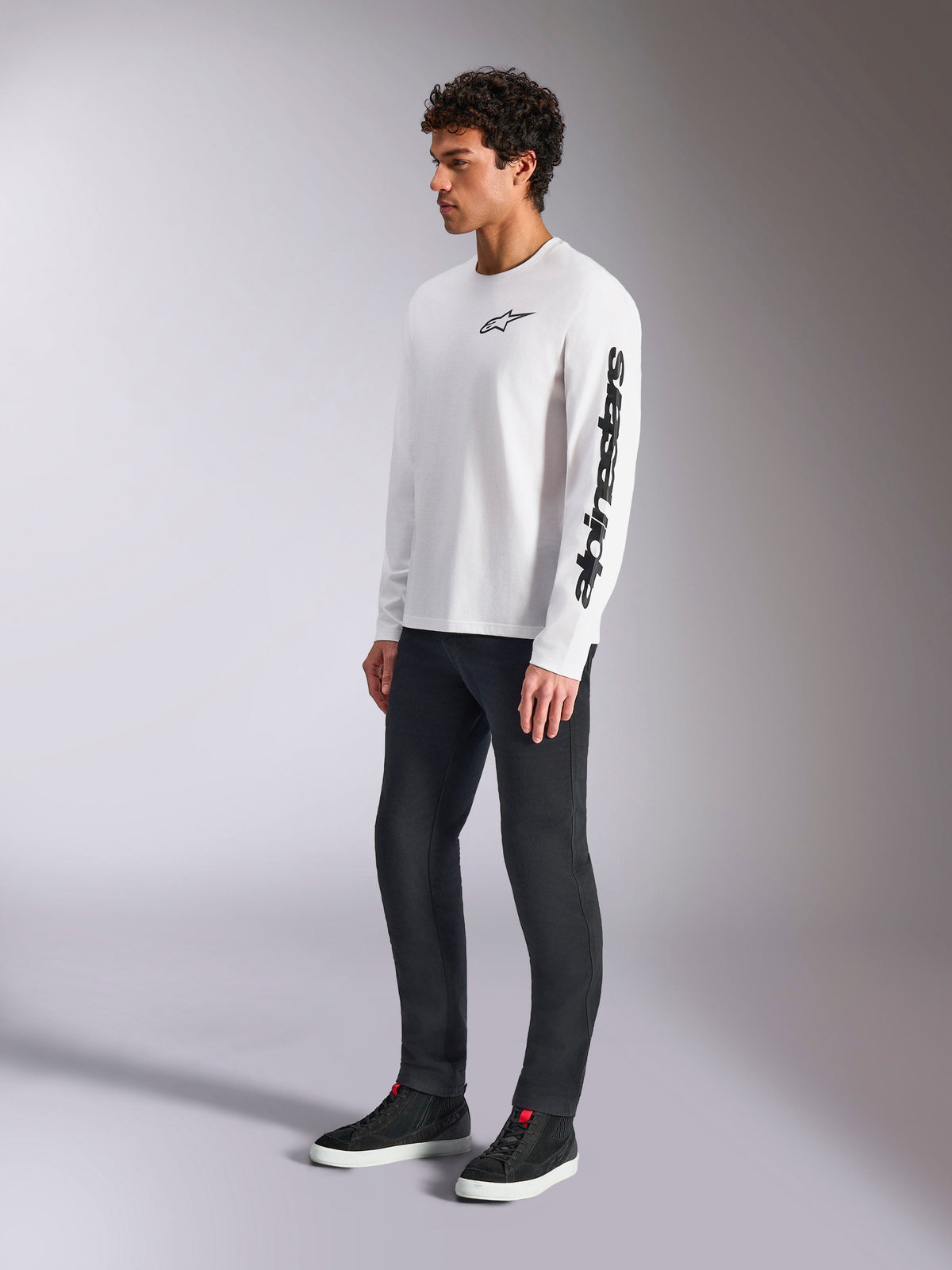 Alpinestars Trackside CSF Tee, Langarm-T-Shirt, Weiß, schwarzes Stern-Logo auf der Brust und Wortmarke auf dem linken Ärmel, getragen von einem männlichen Model mit dunkler Hose und Sneakern, lässige Lifestyle-Sportbekleidung