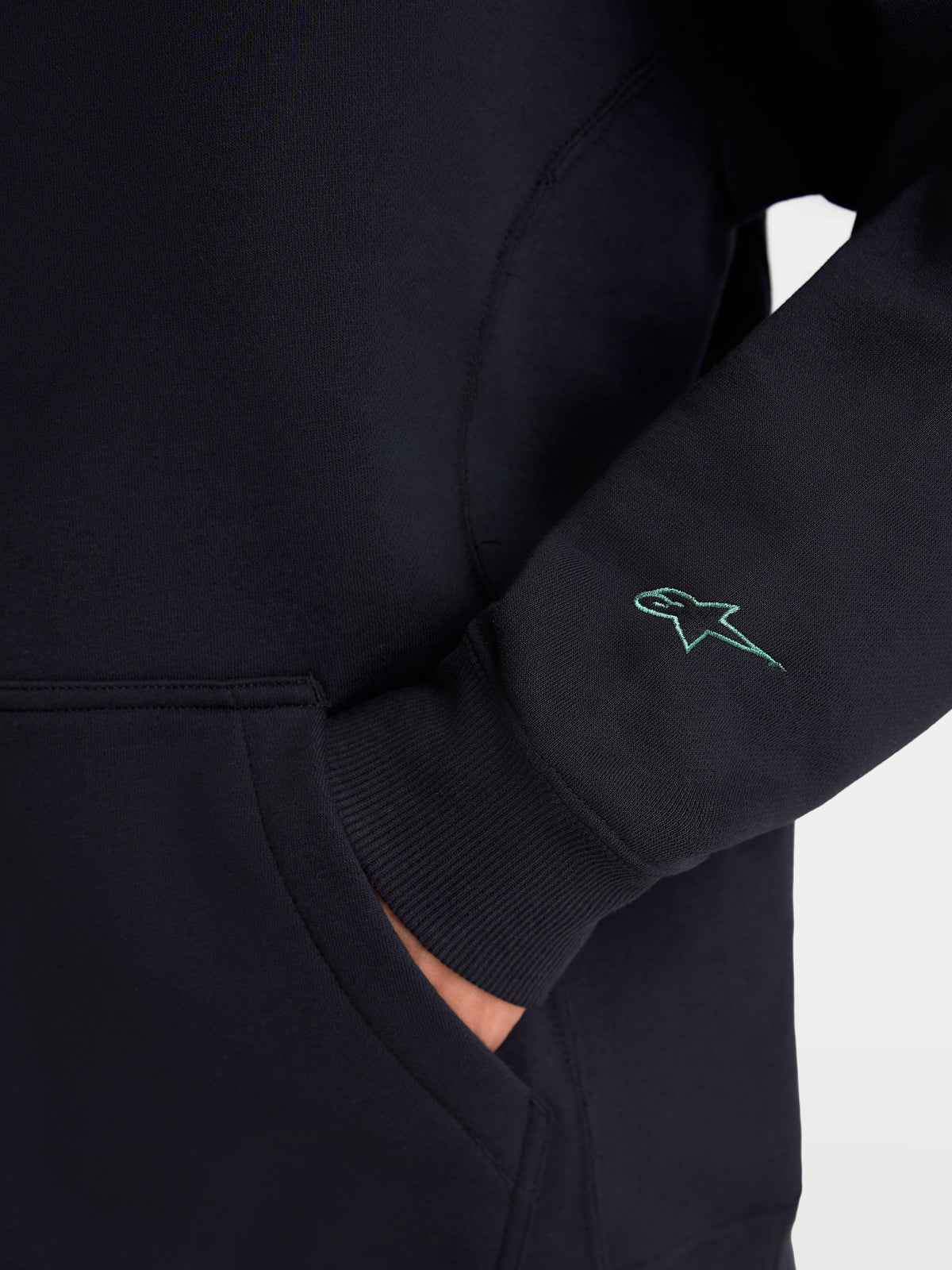 Alpinestars Guise Oversized Crew, Sportswear Fleece-Pullover, Schwarz, Nahaufnahme des bestickten Astars-Logos am Ärmel, mit gerippten Bündchen und Detail der Kängurutasche, Baumwoll- und Recycling-Polyester-Mischung, entspannte Oversized-Passform.