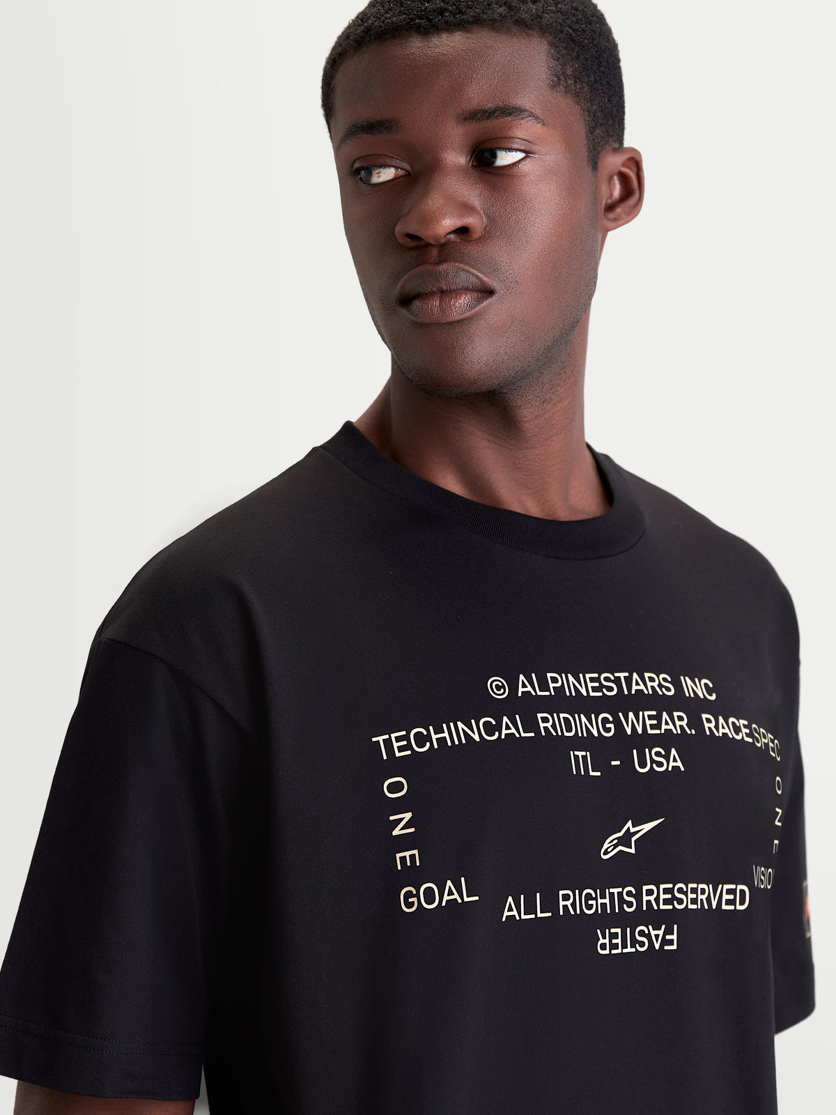 Alpinestars Infinity Oversized CSF T-Shirt, Kurzarm-Sportswear-T-Shirt in Schwarz mit weißer technischer Motorsport-Grafik auf der Brust. Nahaufnahme am Model, Baumwoll-Polyester-Mischung, lässiger Off-Bike-Style.