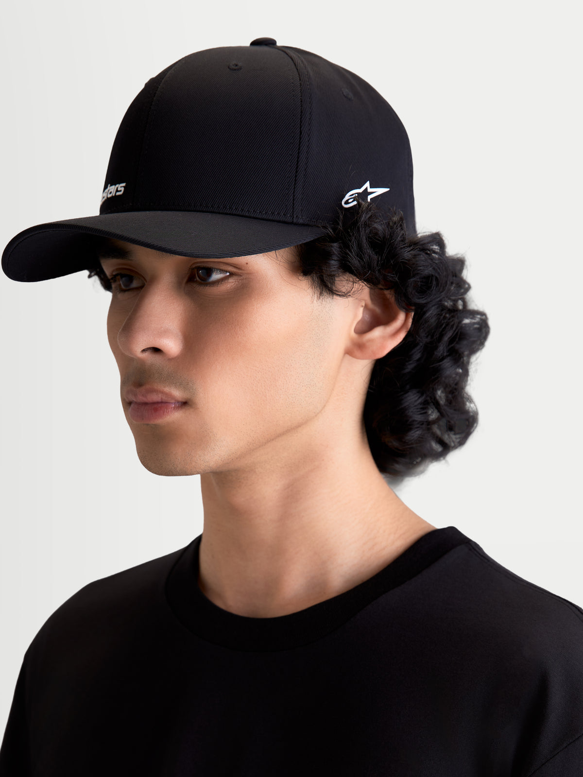 Alpinestars Points Kappe, Sportswear-Kappe mit gebogenem Schirm, Unisex, Schwarz mit weißen Logos, leichtes Nylon-Tactel, Flex-Back-Passform, Seitenansicht am Modell, lässige Motorsport-Lifestyle-Kopfbedeckung.
