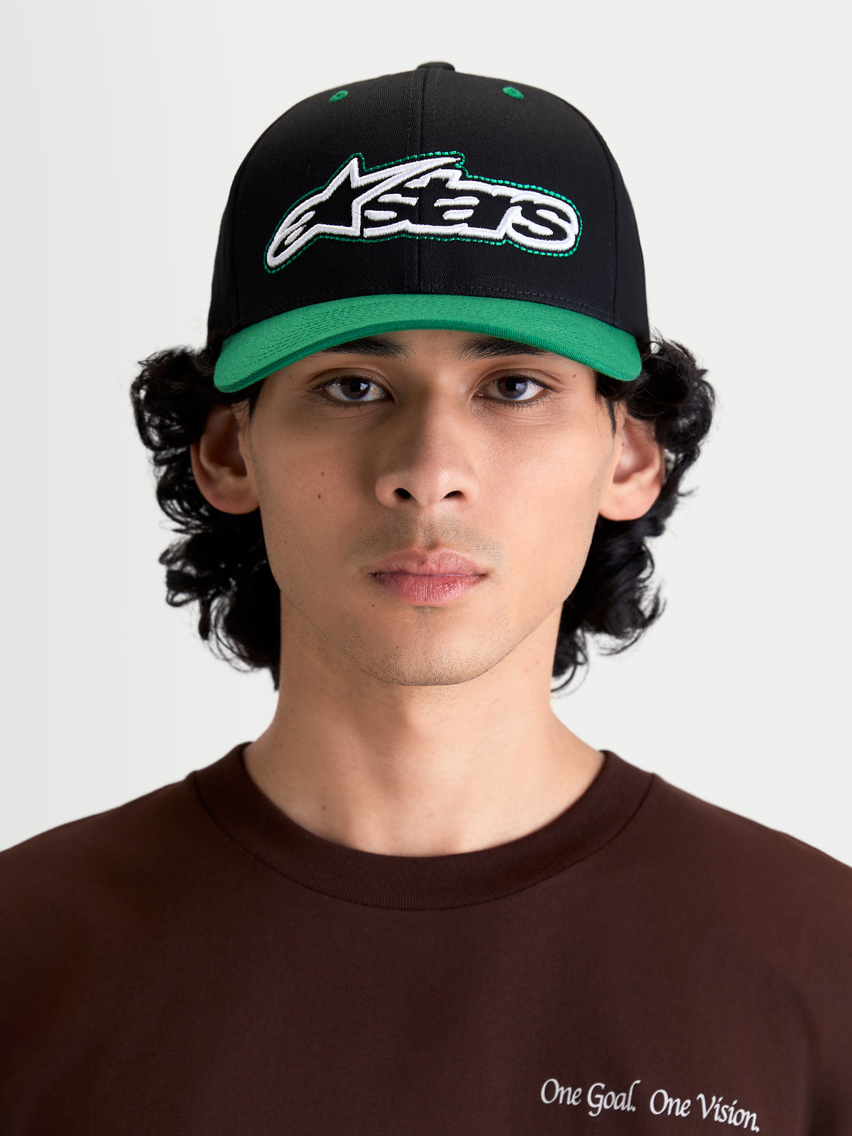 Alpinestars Retro Snapback Hat, Sportswear Lifestyle Cap, Black and Green, featuring a curved bill, structured crown, and front embroidered Astars logo with green running stitch, shown on model front view.