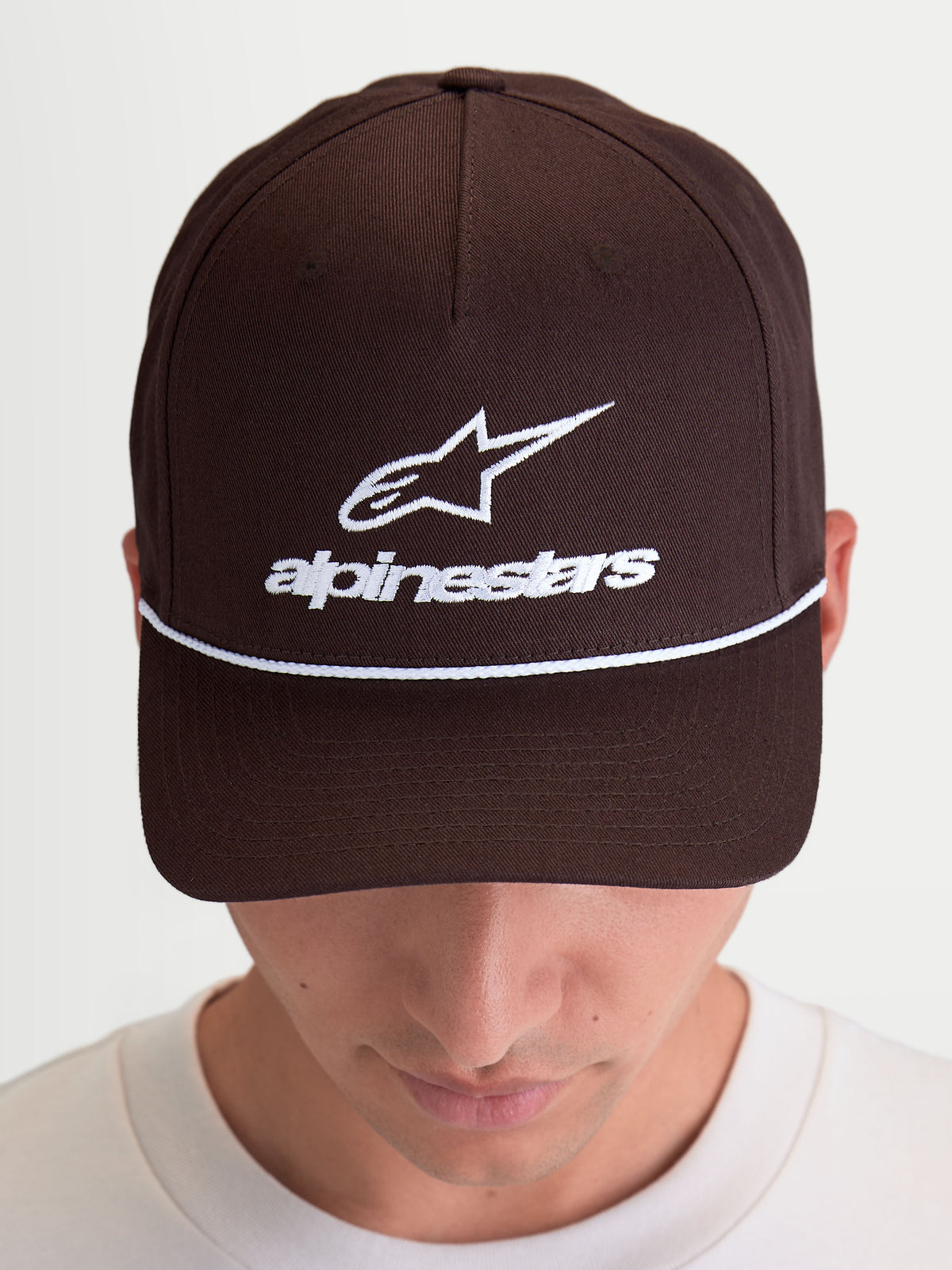 Alpinestars Combo Logo Snapback Kappe, braune Sportswear-Kappe mit weißer Astars-Logo-Stickerei und Wortmarke auf der Vorderseite, gebogener Schirm und strukturierte Krone, hochwertige Twill-Konstruktion, am Modell getragen.