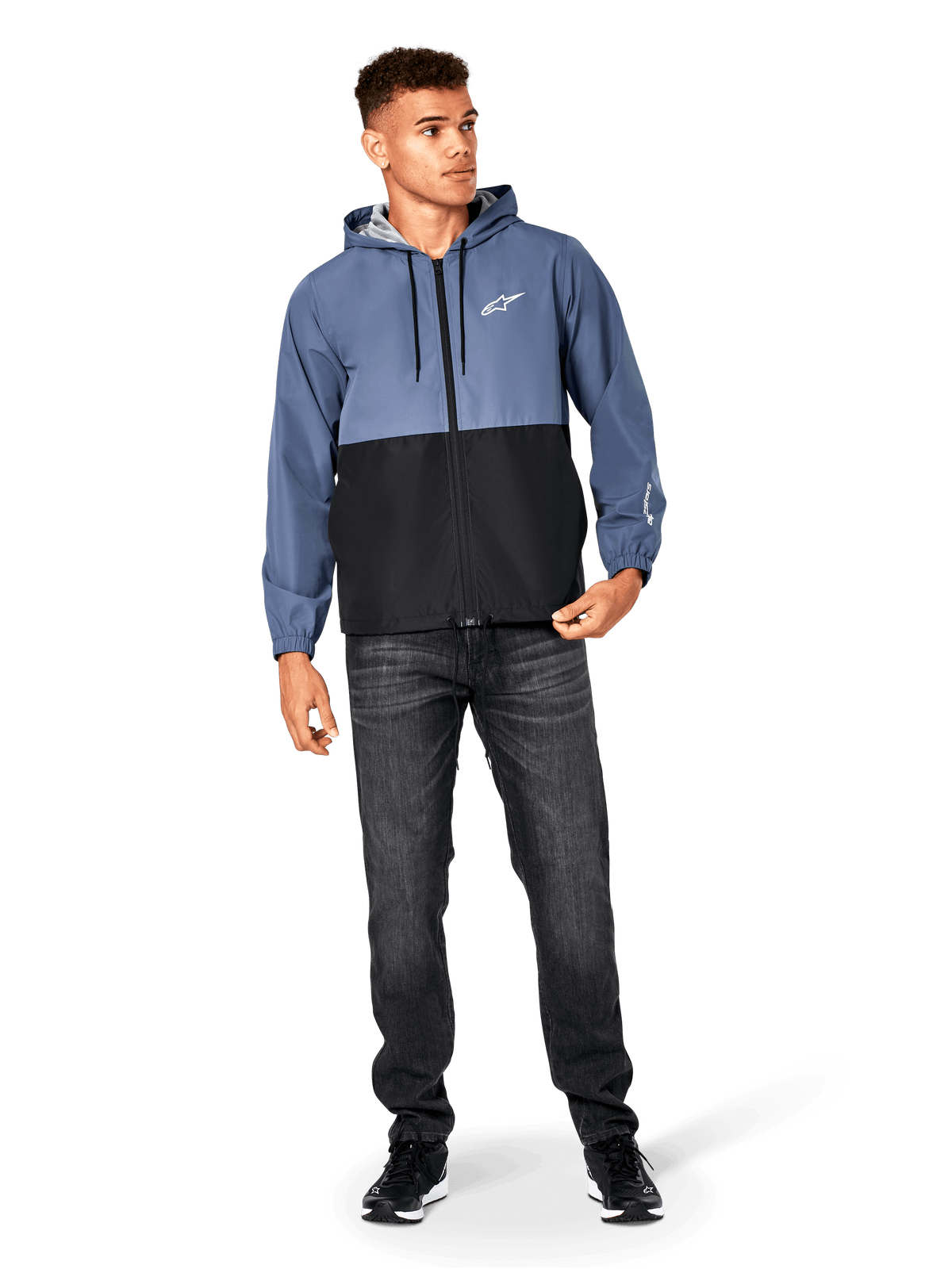 Alpinestars Speeder Windbreaker-Jacke, Schieferblau und Schwarz, leichte Kapuzenjacke mit Mesh-Futter, weißes Stern-Logo auf der Brust, getragen mit schwarzen Jeans und Sneakern, lässiges Motorsport-Streetwear-Design.