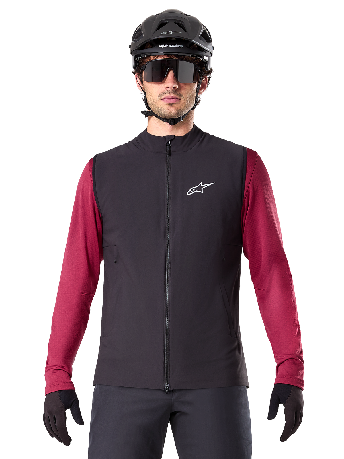 Alpinestars A-Dura Thermoweste, schwarze isolierte Radweste, getragen von einem Modell mit weinrotem Langarmtrikot, schwarzem MTB-Helm und Sonnenbrille, mit weißem Logo auf der Brust, leichter Wärmeschutz fürs Mountainbiken