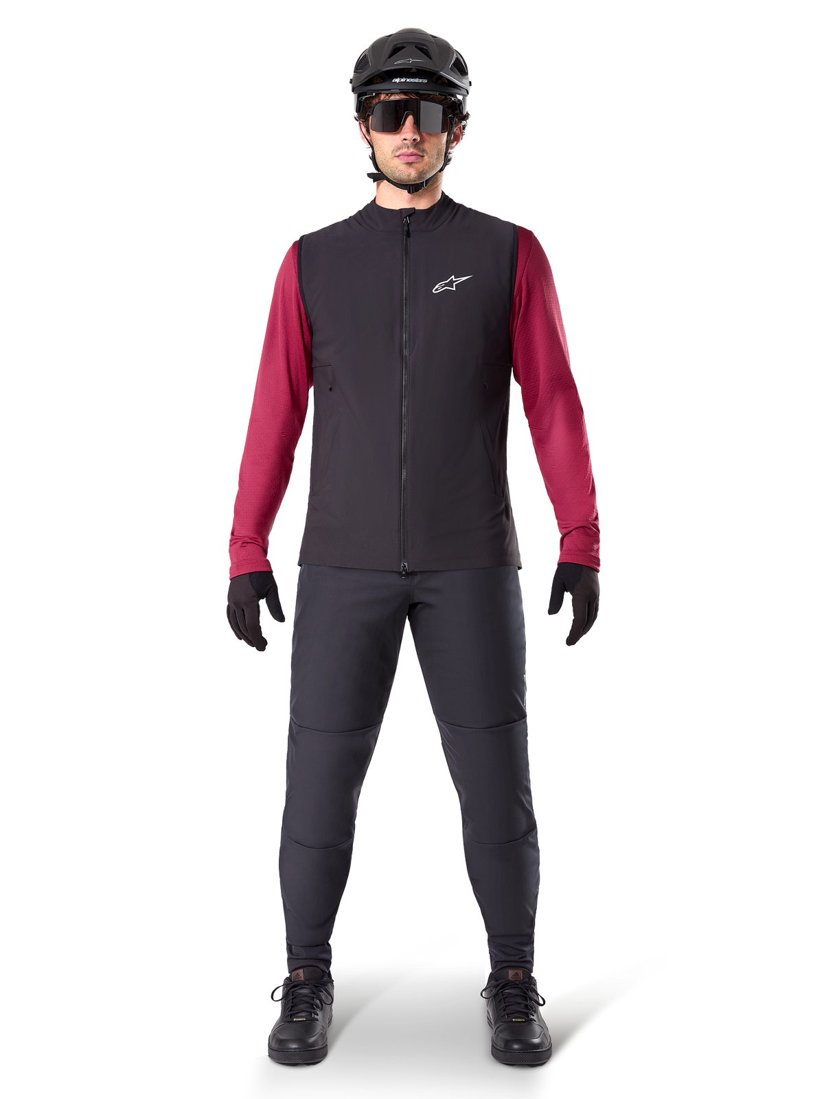 Alpinestars A-Dura Thermoweste, schwarze Radweste getragen über einem weinroten Langarmtrikot, kombiniert mit dunkelgrauer MTB-Hose, schwarzem Helm und Sonnenbrille, technische Mountainbike-Bekleidung für Fahrten bei kaltem Wetter