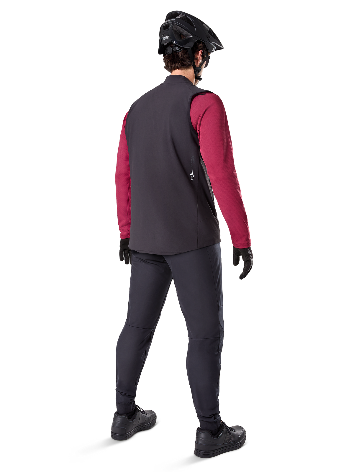 Alpinestars A-Dura Thermoweste, schwarze Fahrradweste, Rückansicht an einem Model mit weinrotem Langarm-Trikot und schwarzer Fahrradhose, kombiniert mit schwarzem Mountainbike-Helm und Handschuhen, technische Ausrüstung für Fahrten bei kaltem Wetter.