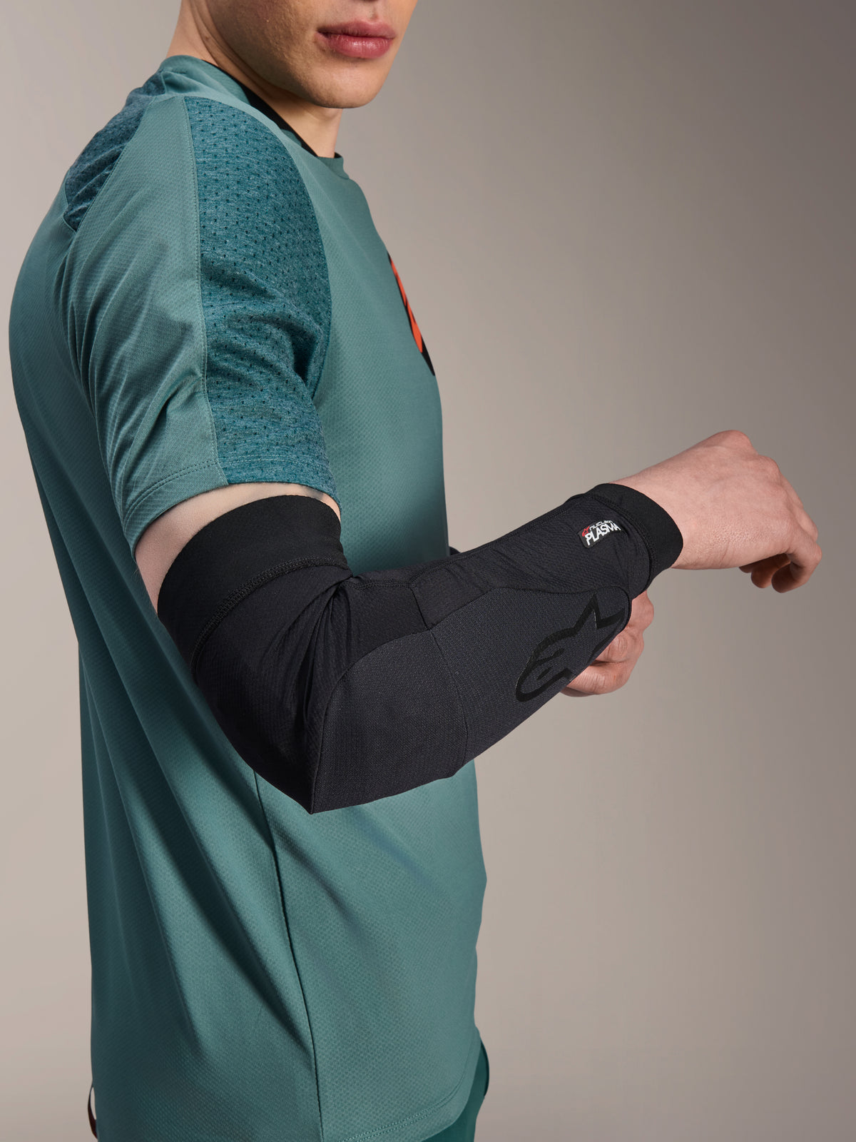 Alpinestars A-Motion Plasma Ellbogenärmel, Radsport-Ellbogenprotektor, Schwarz, getragen von einem Fahrer mit einem blaugrünen Trikot, mit Alpinestars-Logo und Nucleon Plasma-Branding, schlankes und atmungsaktives Design für MTB-Schutz