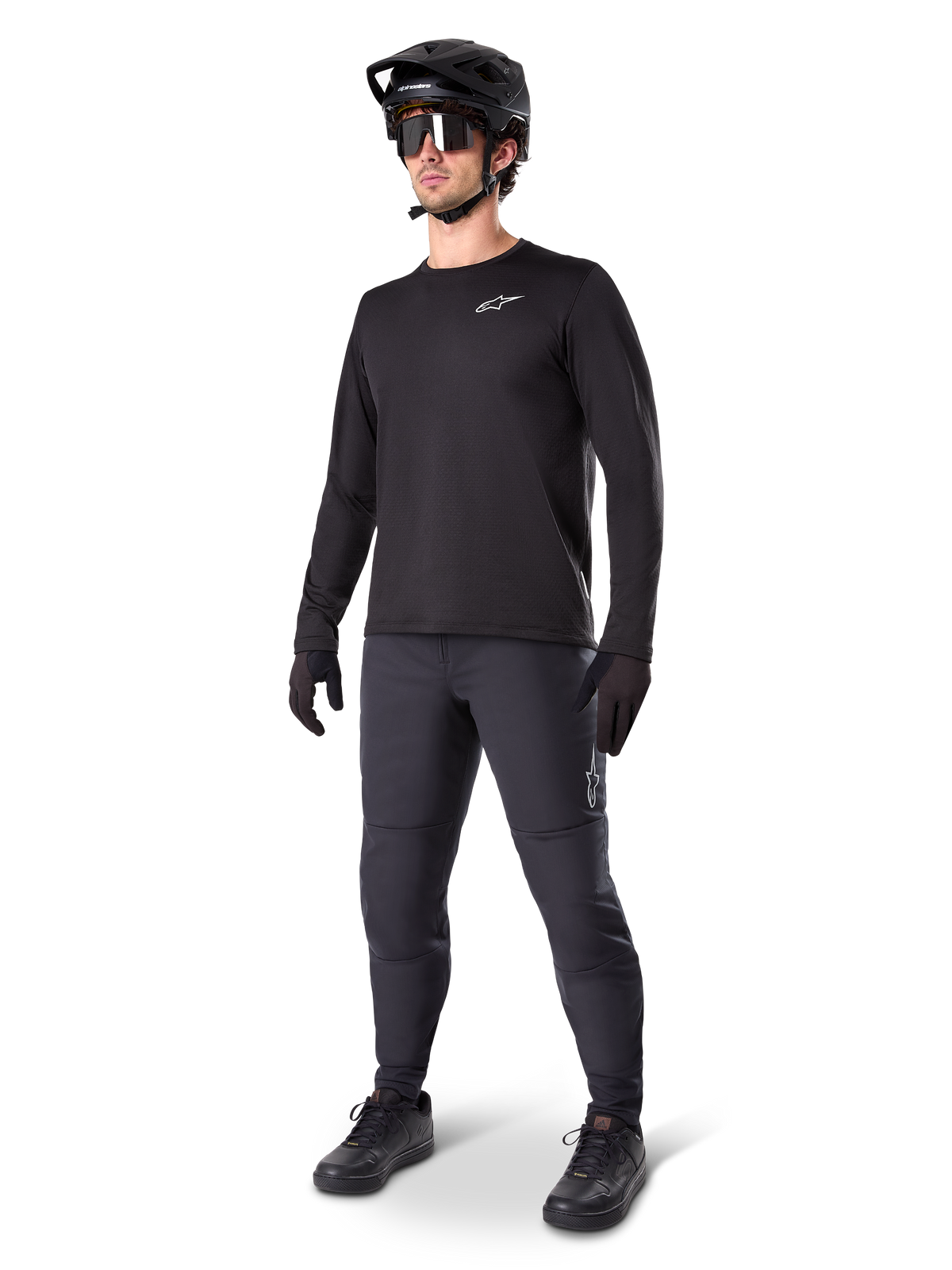 Mountain bike rider wearing Alpinestars A-Dura Thermal Pants, Black, styled with a black long-sleeve jersey, black helmet, and sunglasses, featuring a silver Alpinestars logo on the left thigh, designed for cold-weather trail riding