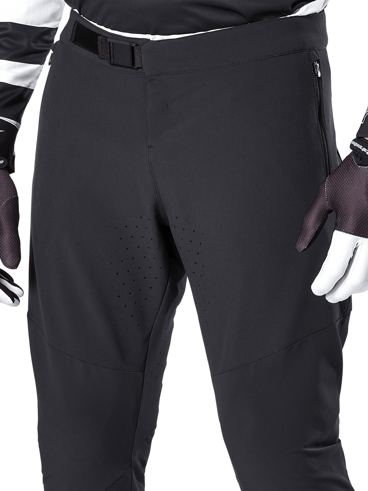 Alpinestars A-Aria Elite Hose, schwarze Mountainbike-Hose, Nahaufnahme von Taille und Oberschenkeln mit magnetischem Schnallenverschluss und lasergeschnittenen Belüftungslöchern, kombiniert mit Fahrradhandschuhen