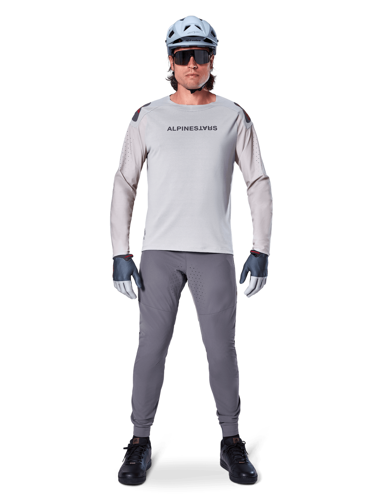 Alpinestars A-Aria Elite Hose, dunkelgraue Mountainbike-Hose, getragen von einem Fahrer in hellgrauem Langarmtrikot, hellblauem Helm und schwarzen Schuhen, mit sichtbaren Laserperforationen an den Beininnenseiten und schmaler Performance-Passform.